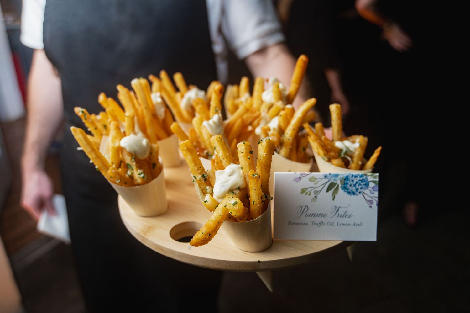 Golden french fries served in individual paper cones on a wooden serving tray with a decorative place card.