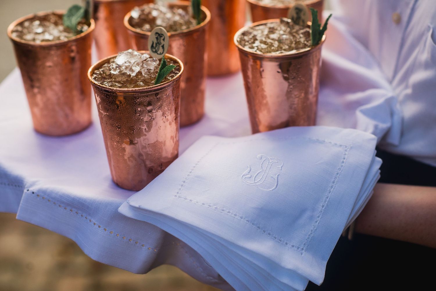 Several copper Moscow Mule mugs filled with cocktails and garnished with mint leaves sit on a white tablecloth.