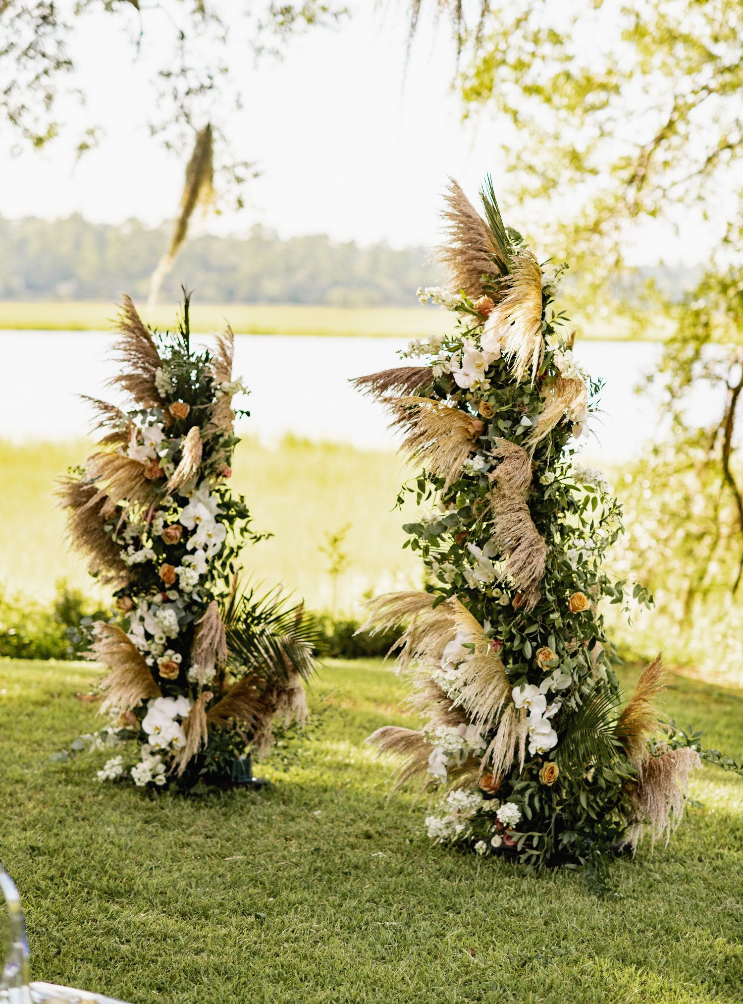 Elegant boho floral arrangements with pampas grass and white flowers displayed on grass in natural outdoor setting.