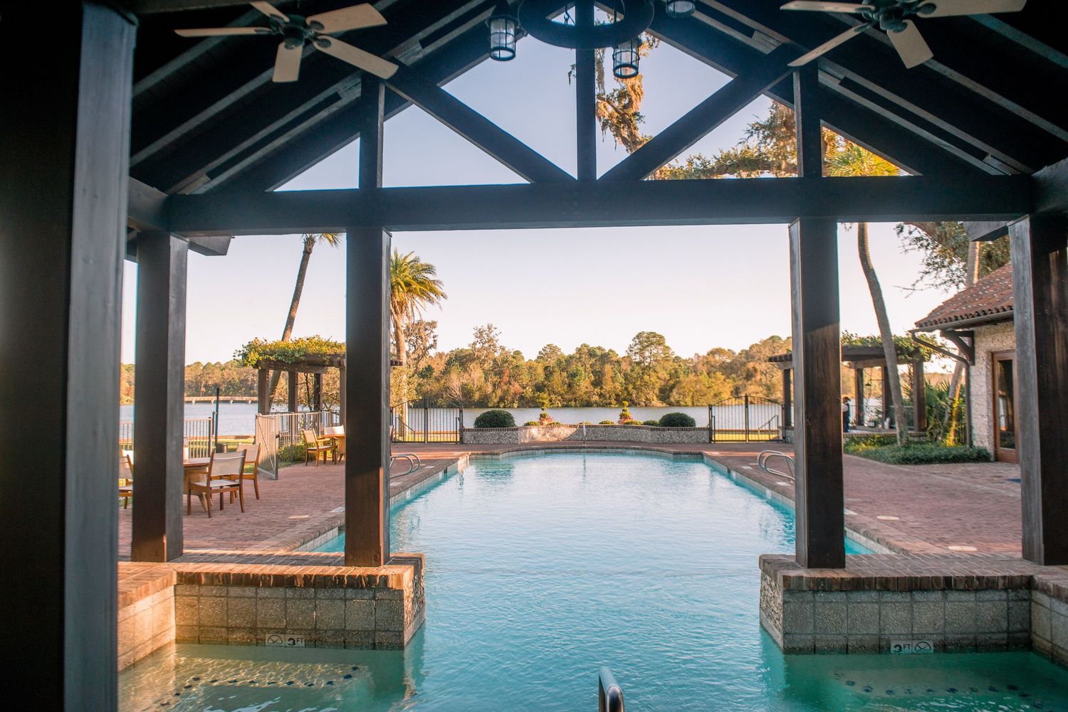 Wooden pier walkway with black beams extends over turquoise water during golden sunset at a coastal marina.