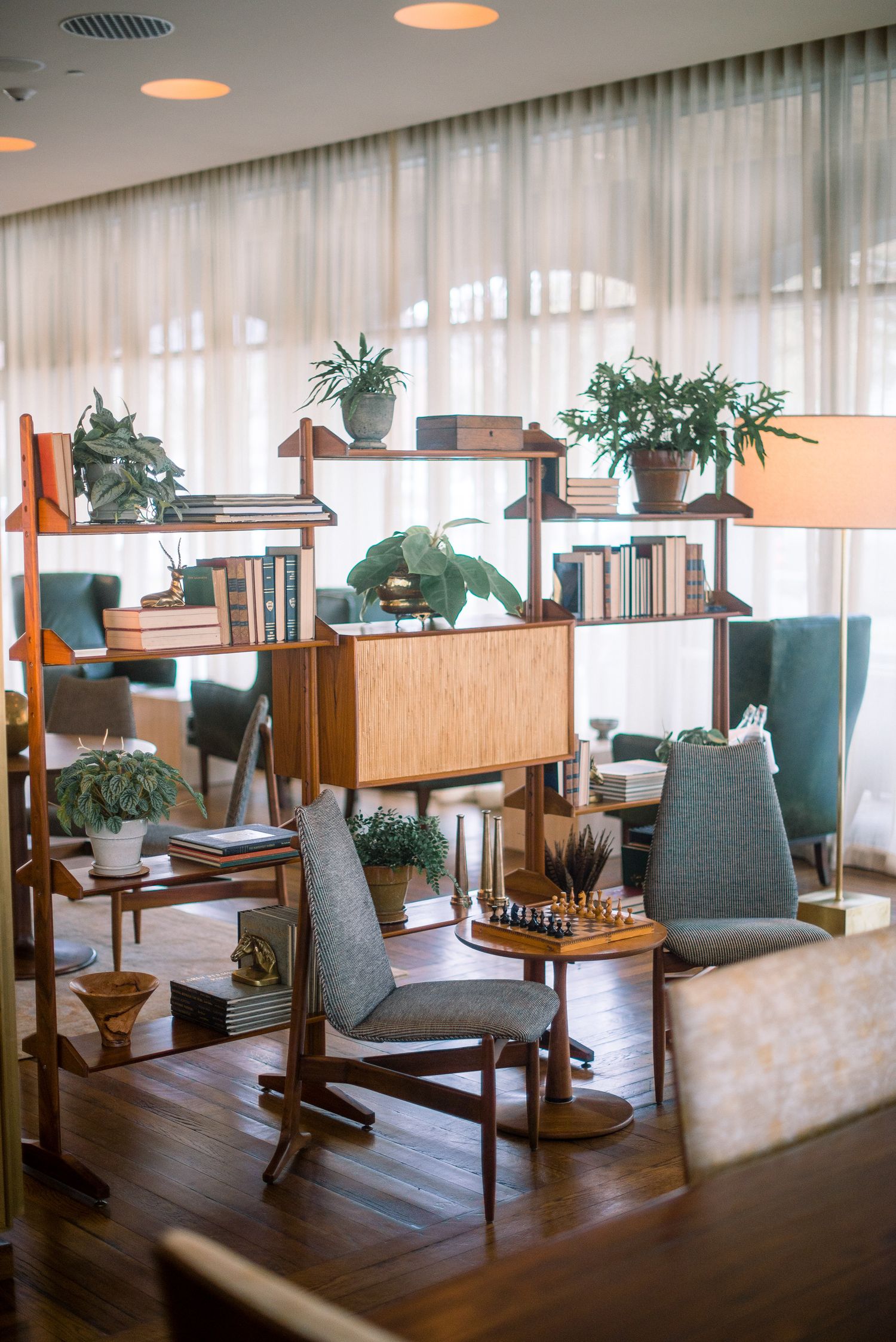 Modern restaurant interior with grey upholstered chairs, wooden tables, and hanging pendant lights in a bright space.