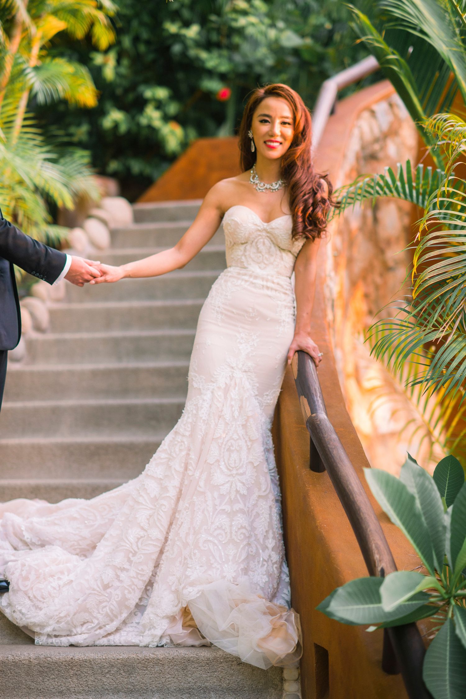 Elegant lace wedding dress photographed in a tropical garden setting with palm trees.
