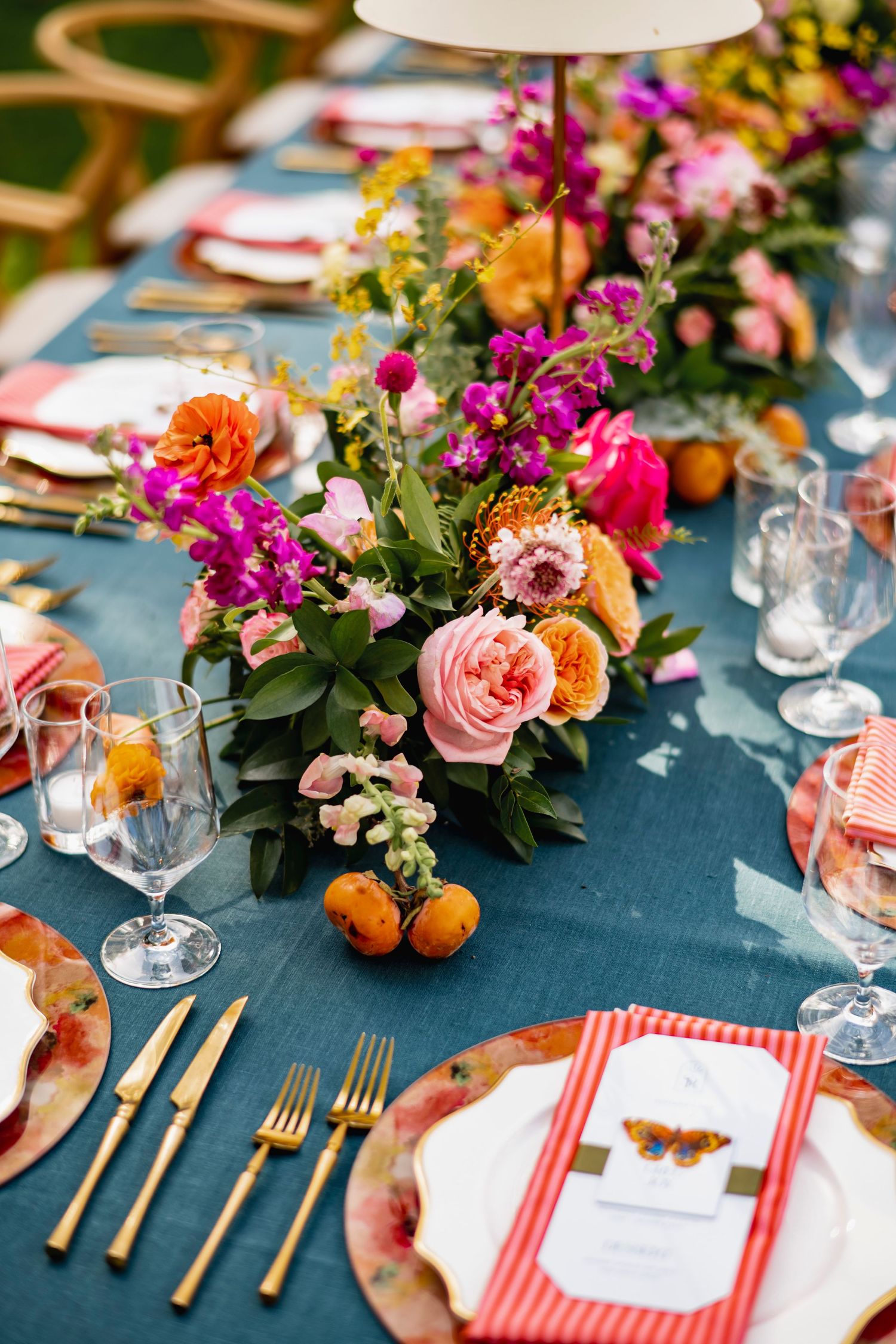 Wedding table setting with pink and orange florals, gold cutlery, and navy blue linens.