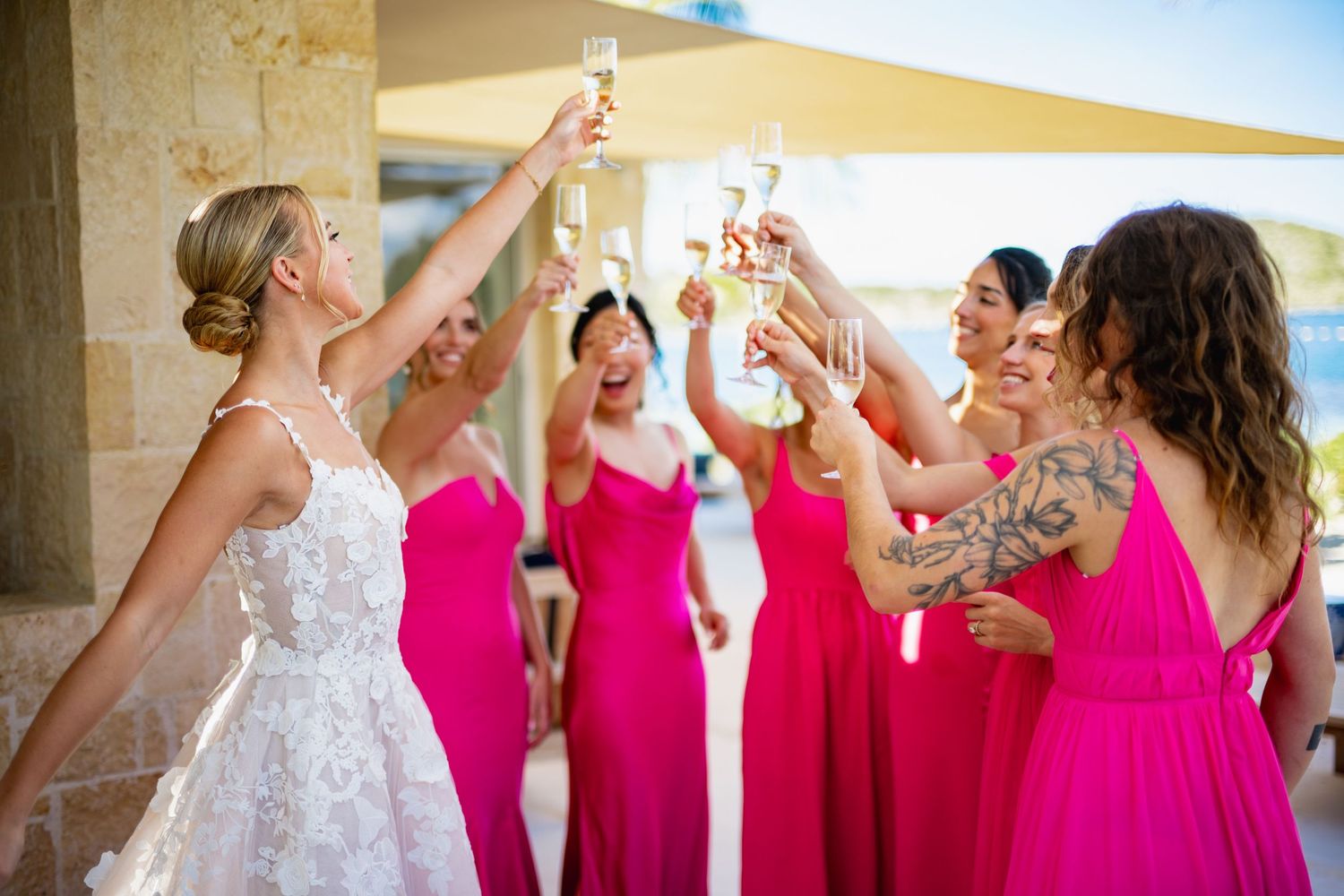 Wedding party in pink dresses toasts with champagne glasses during celebration.