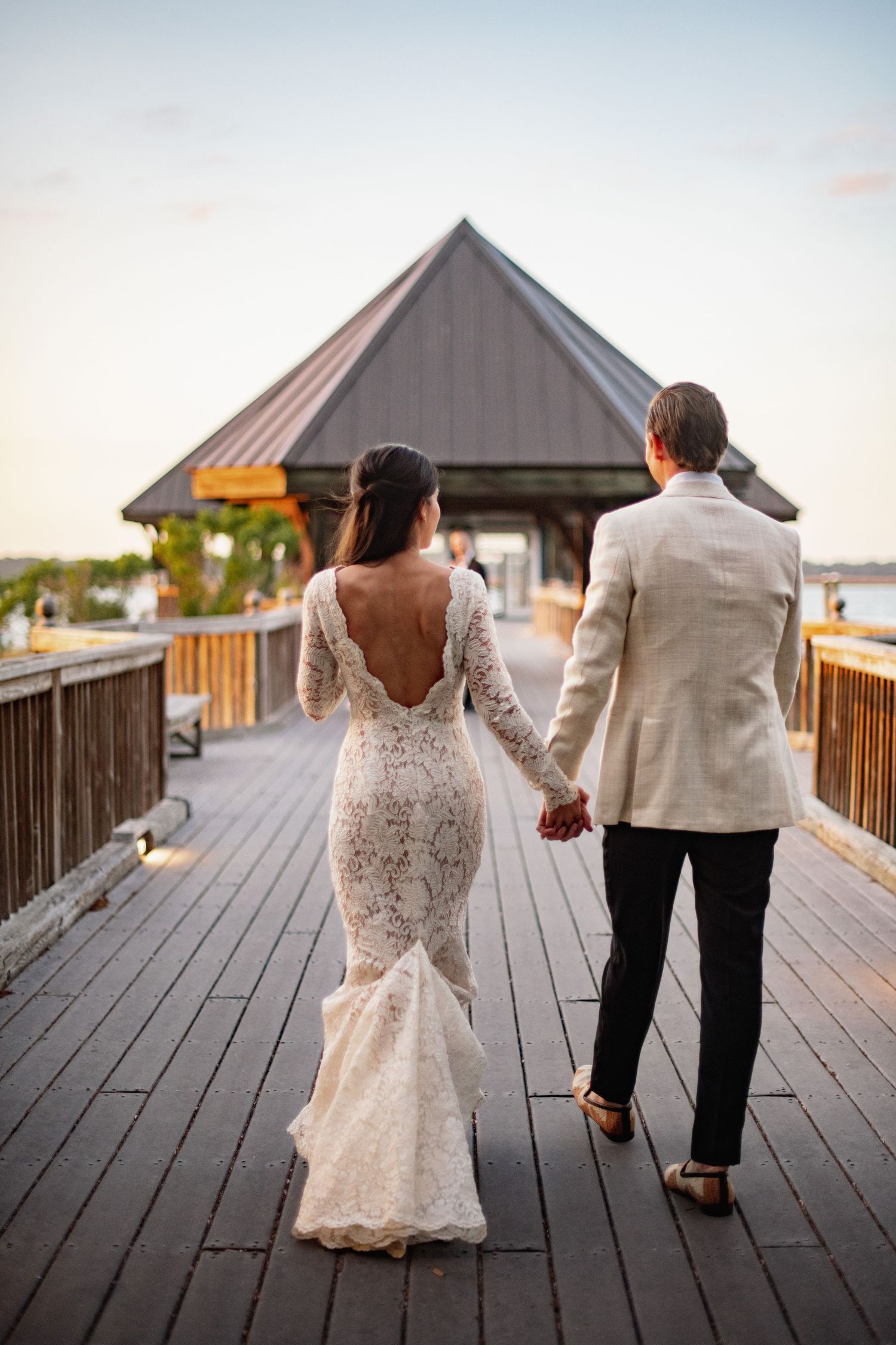 Couple walking together on a wooden boardwalk at sunset with gazebos in the background.
