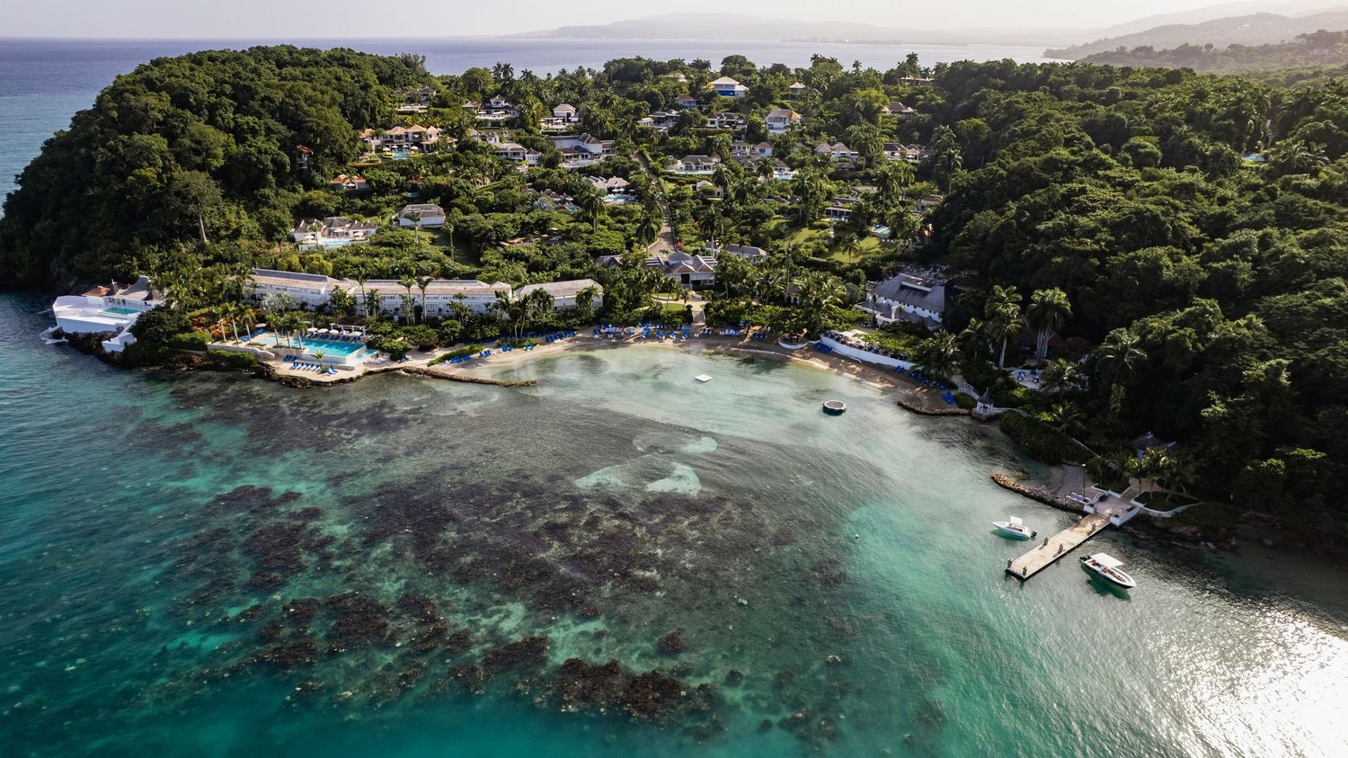 Aerial panoramic view of a tropical coastline with turquoise waters, coral reefs, and lush green vegetation.