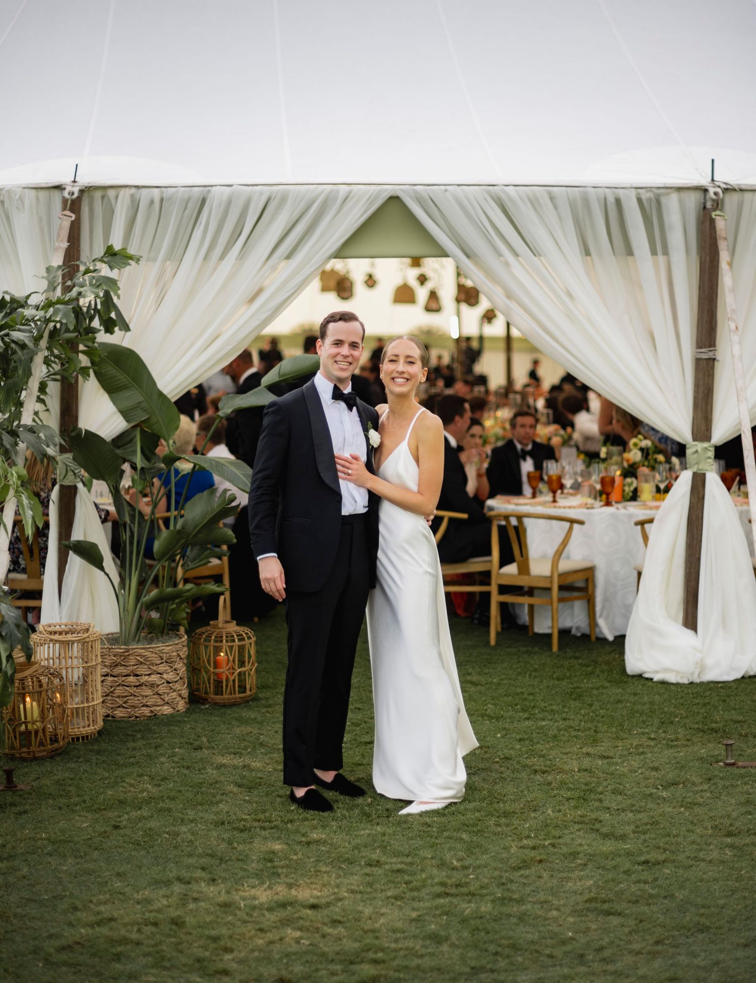 A couple shares a romantic dance moment under white flowing tent drapes at an elegant outdoor wedding reception.