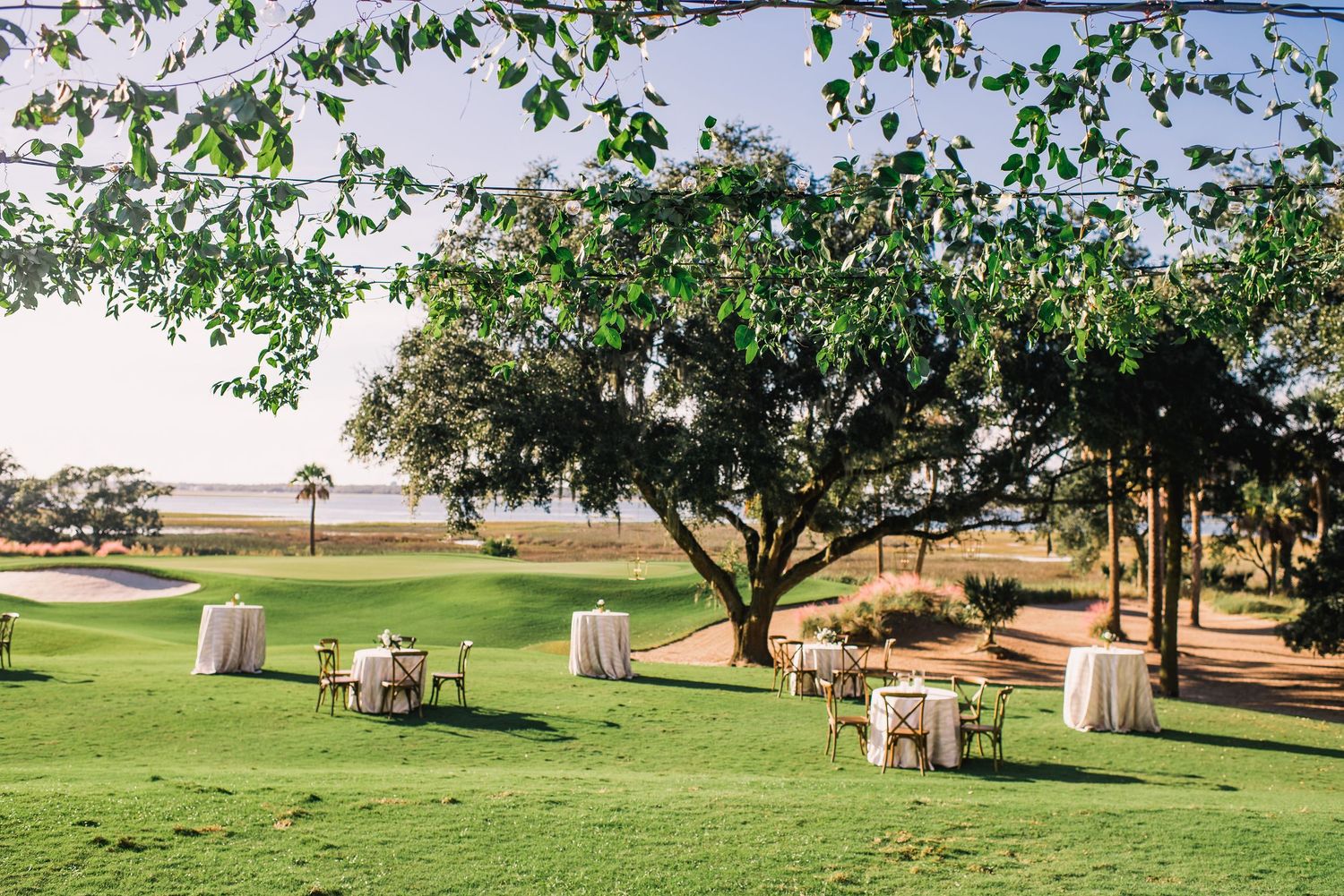 Outdoor wedding ceremony setup with white chairs and fabric draping between trees on a lush green lawn.