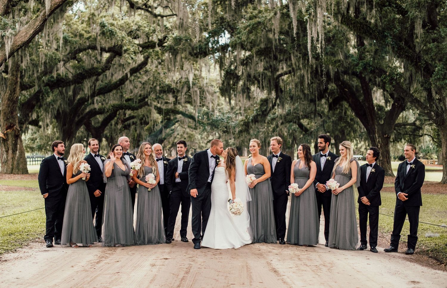 Wedding party poses under Spanish moss draped oak trees in outdoor garden setting.