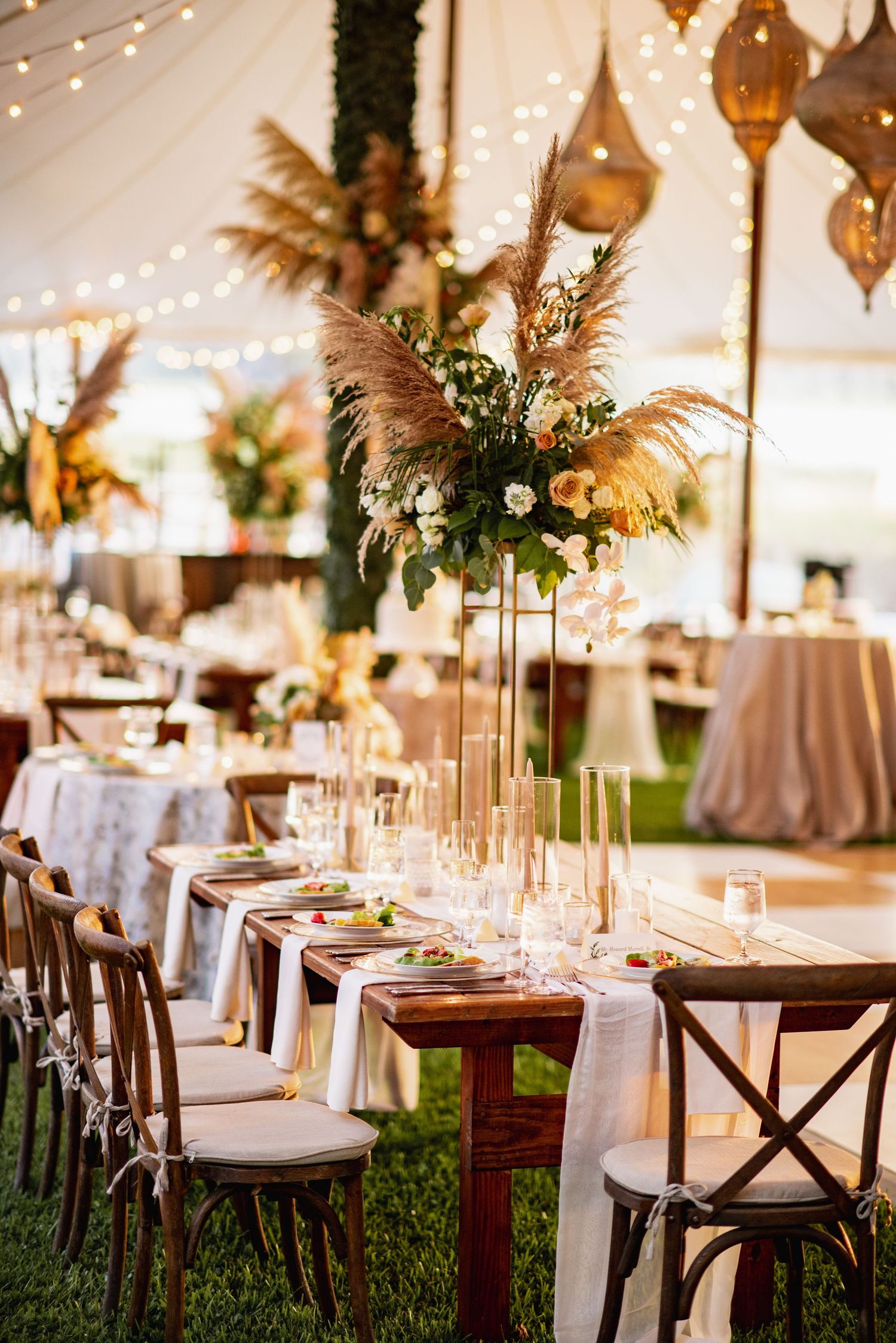 Elegant wedding reception setup with rustic wood tables, string lights, and floral centerpieces in a tent venue.