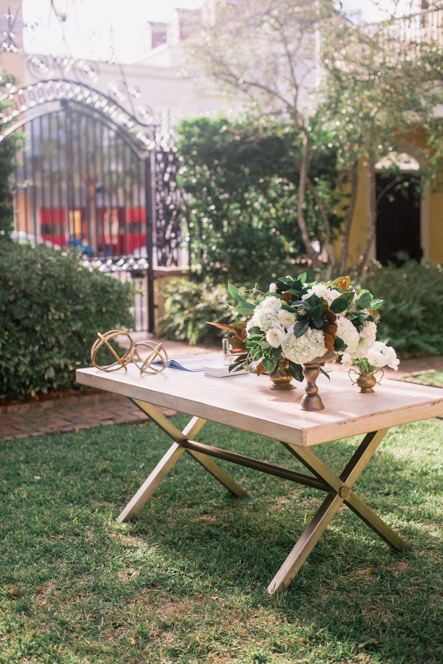 Rustic wooden picnic table with white floral centerpieces arranged in a row on a grassy lawn.