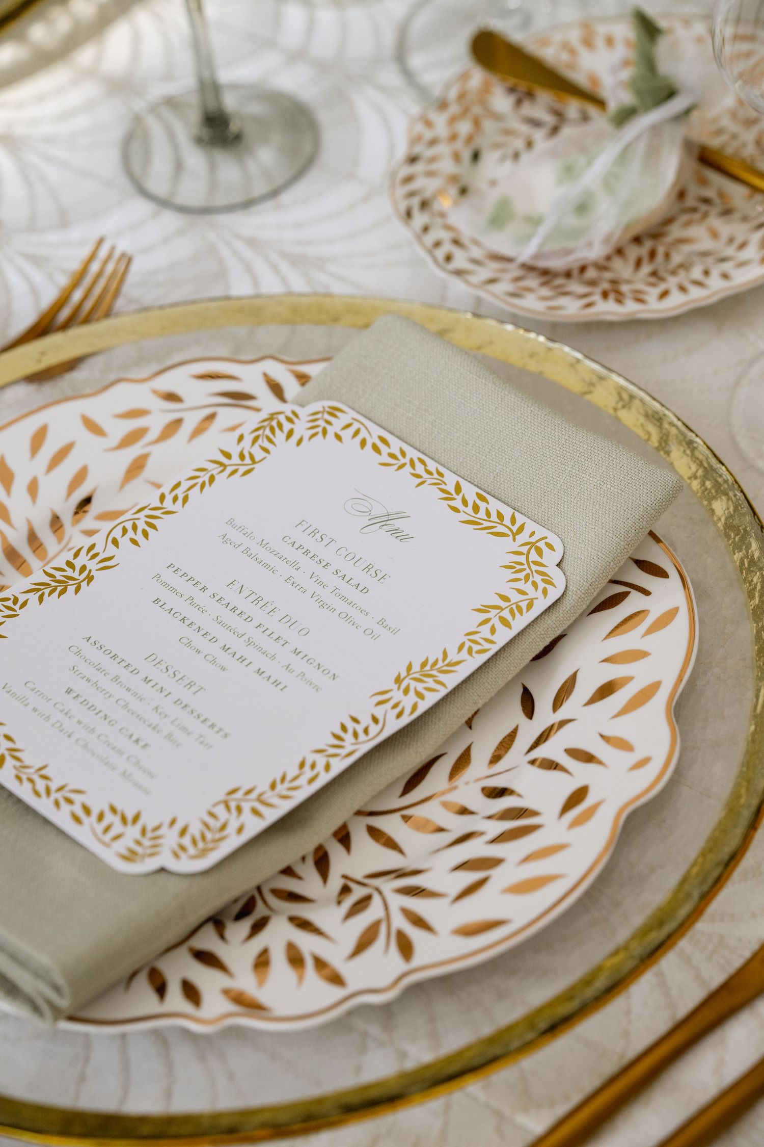 Elegant gold-rimmed place settings with ornate menu cards featuring leaf designs.