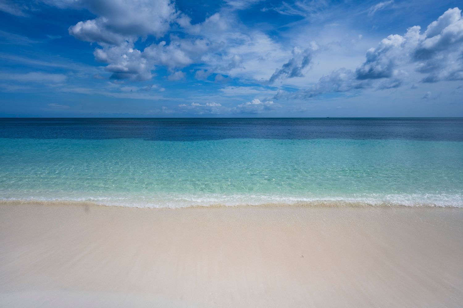 Stunning panoramic view of a pristine tropical beach with turquoise waters and white sand under a blue cloudy sky.