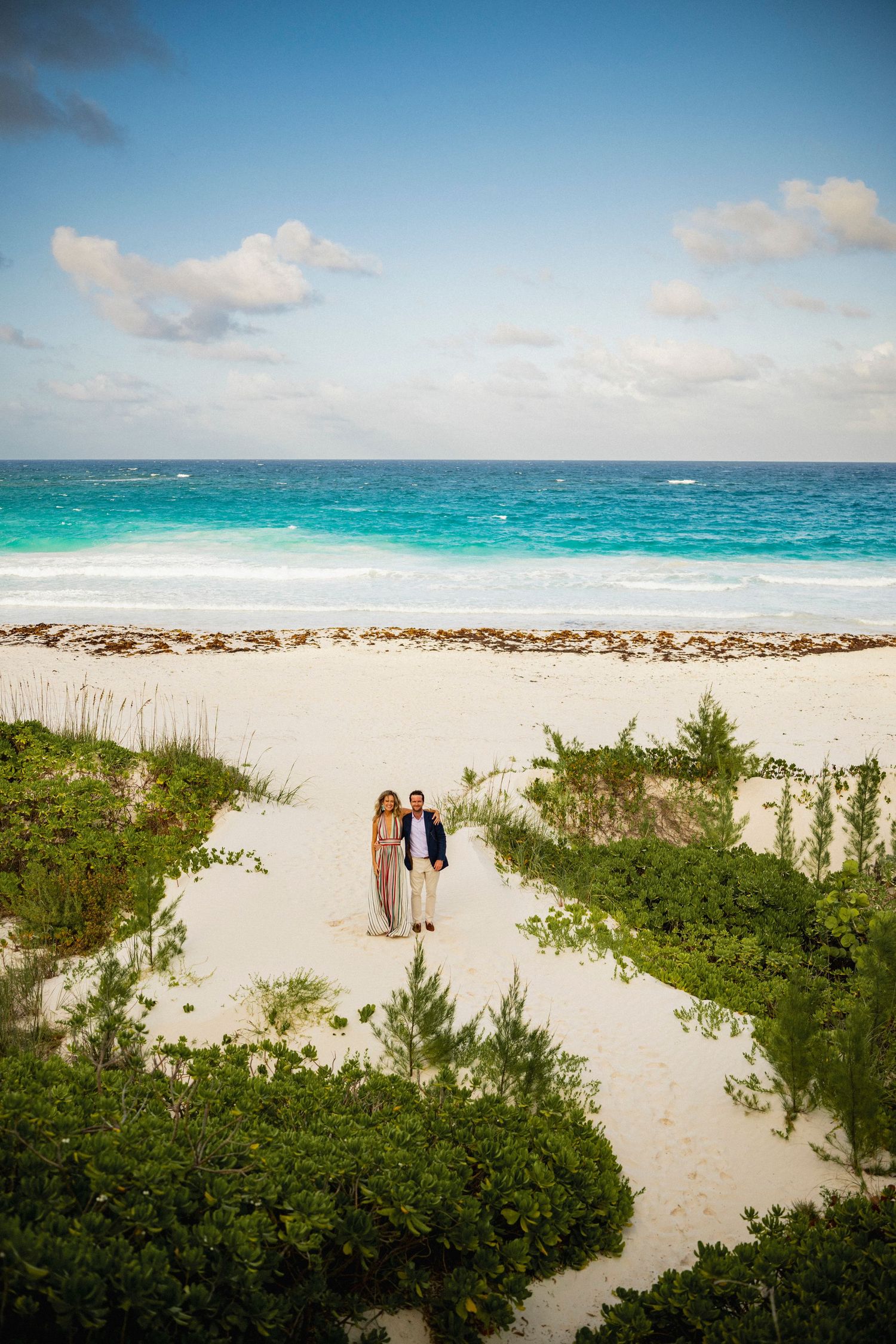 Scenic beach path through coastal vegetation leads to turquoise Caribbean waters under partly cloudy skies.