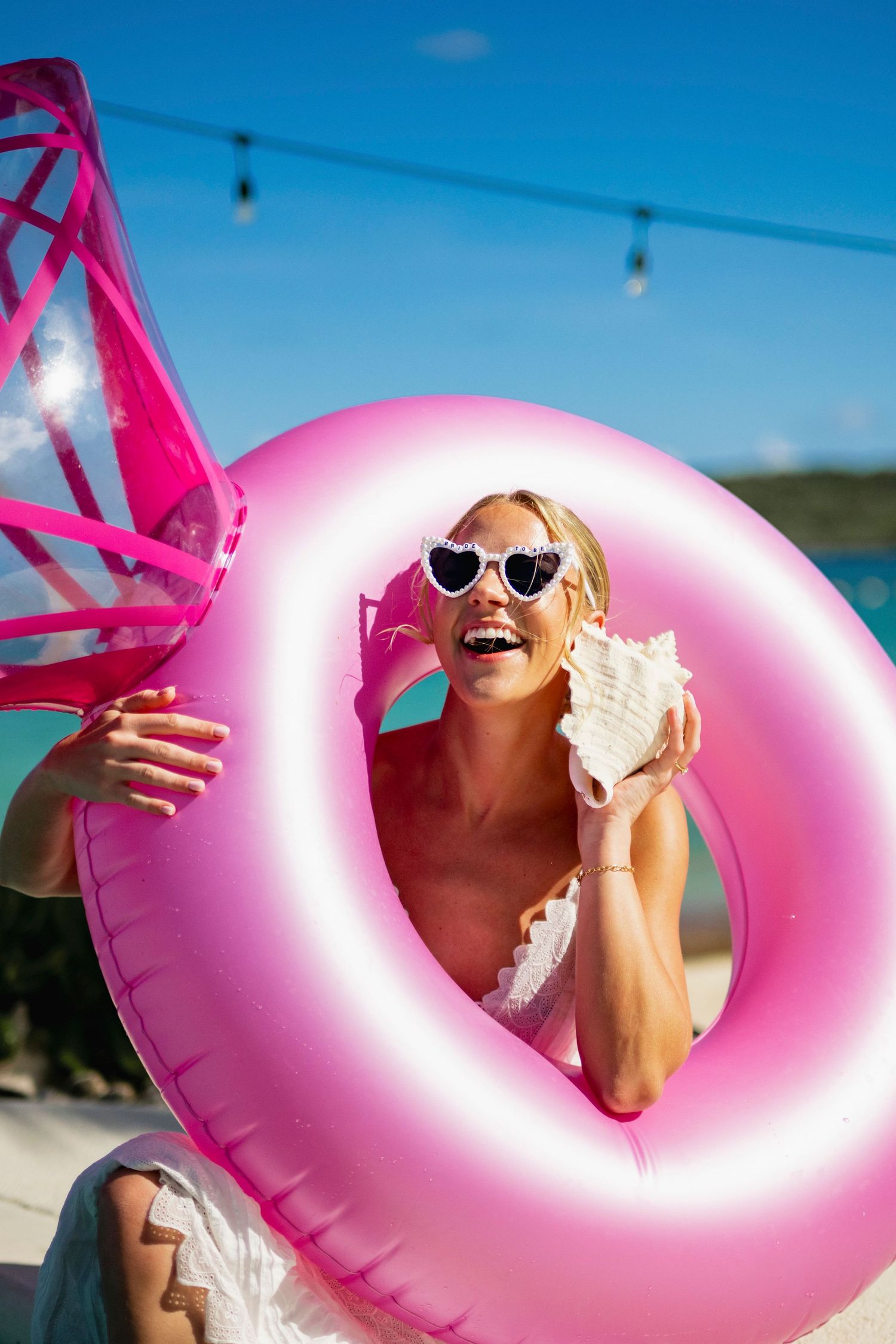Person with sunglasses enjoying summer fun with pink pool float against bright blue sky.