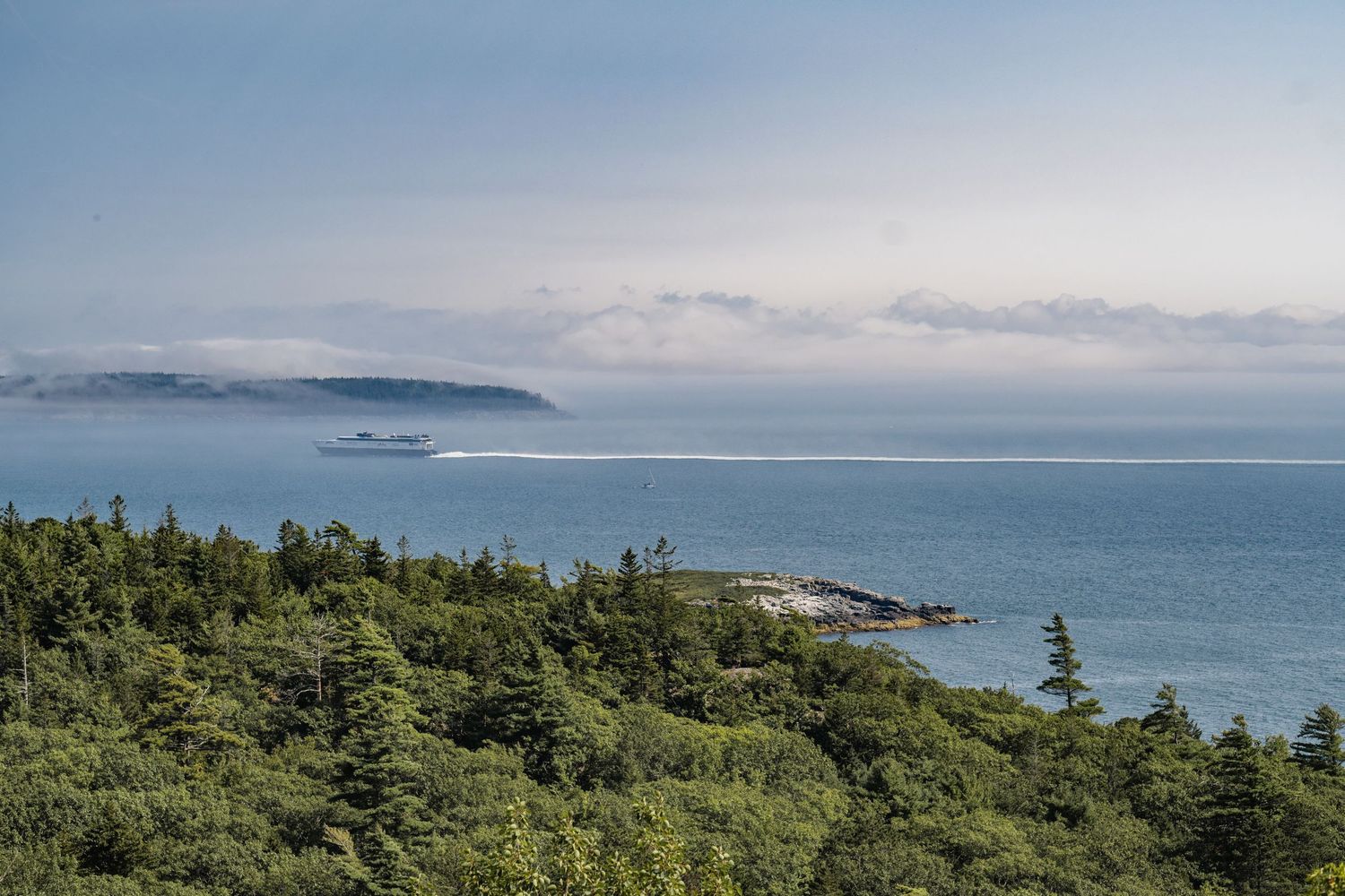 Scenic coastal landscape in Maine's Acadia national park with green forested hills overlooking a misty ocean bay.