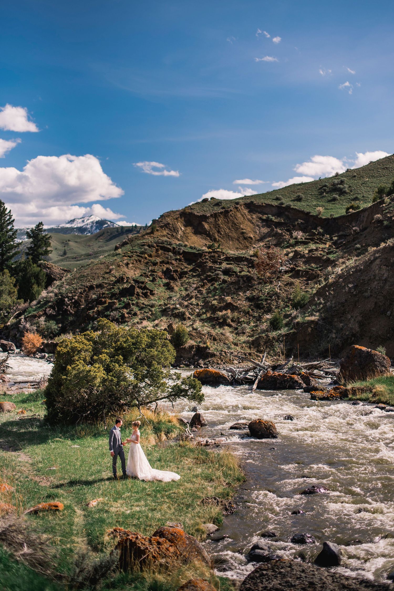 A wedding couple poses in a dramatic mountain landscape with rushing water and rocky terrain.