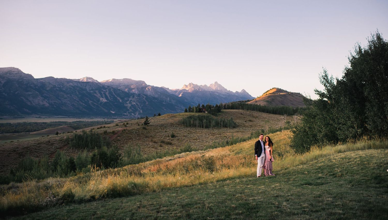 A scenic mountain landscape panorama with rolling hills and golden grass at sunset.