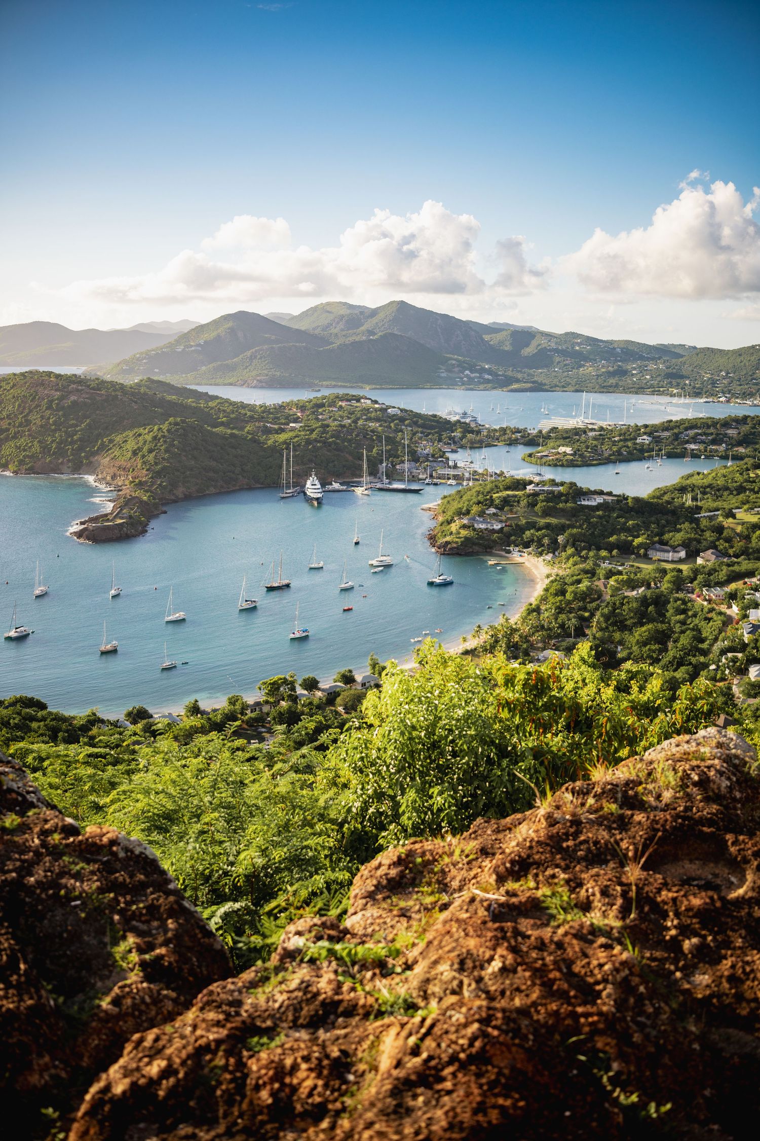 Panoramic view of English Harbour in Antigua with sailboats anchored in turquoise waters surrounded by lush hills.