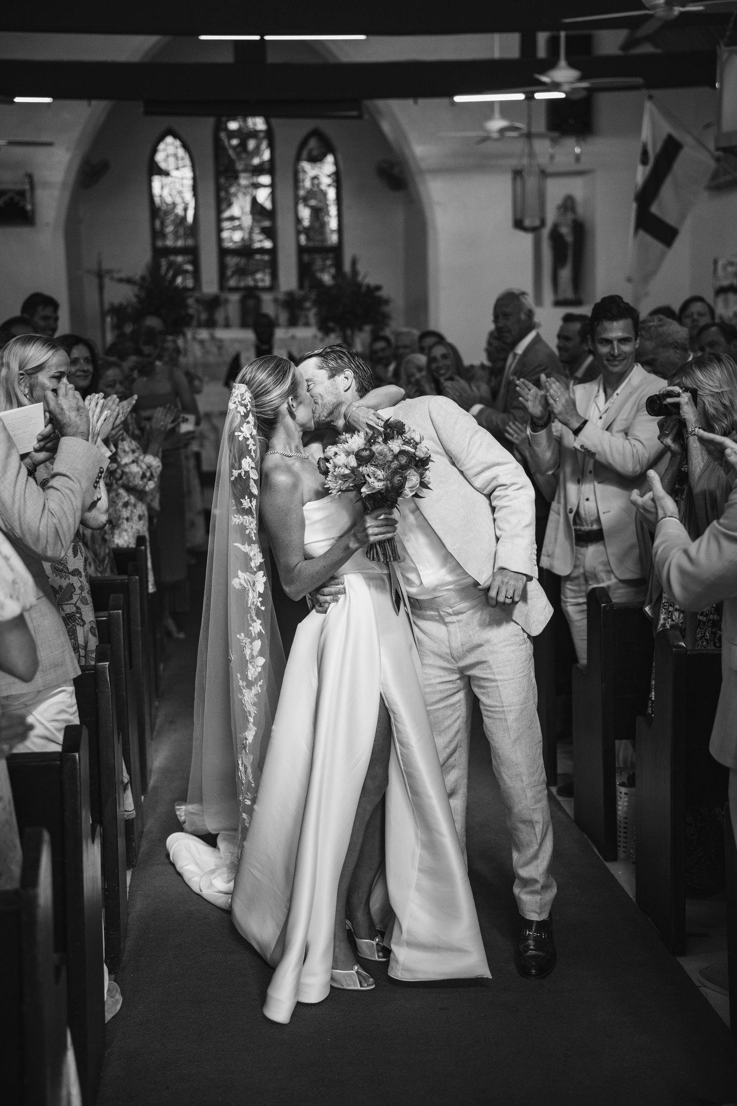 Wedding guests in all-white attire dancing in a line during a celebration.