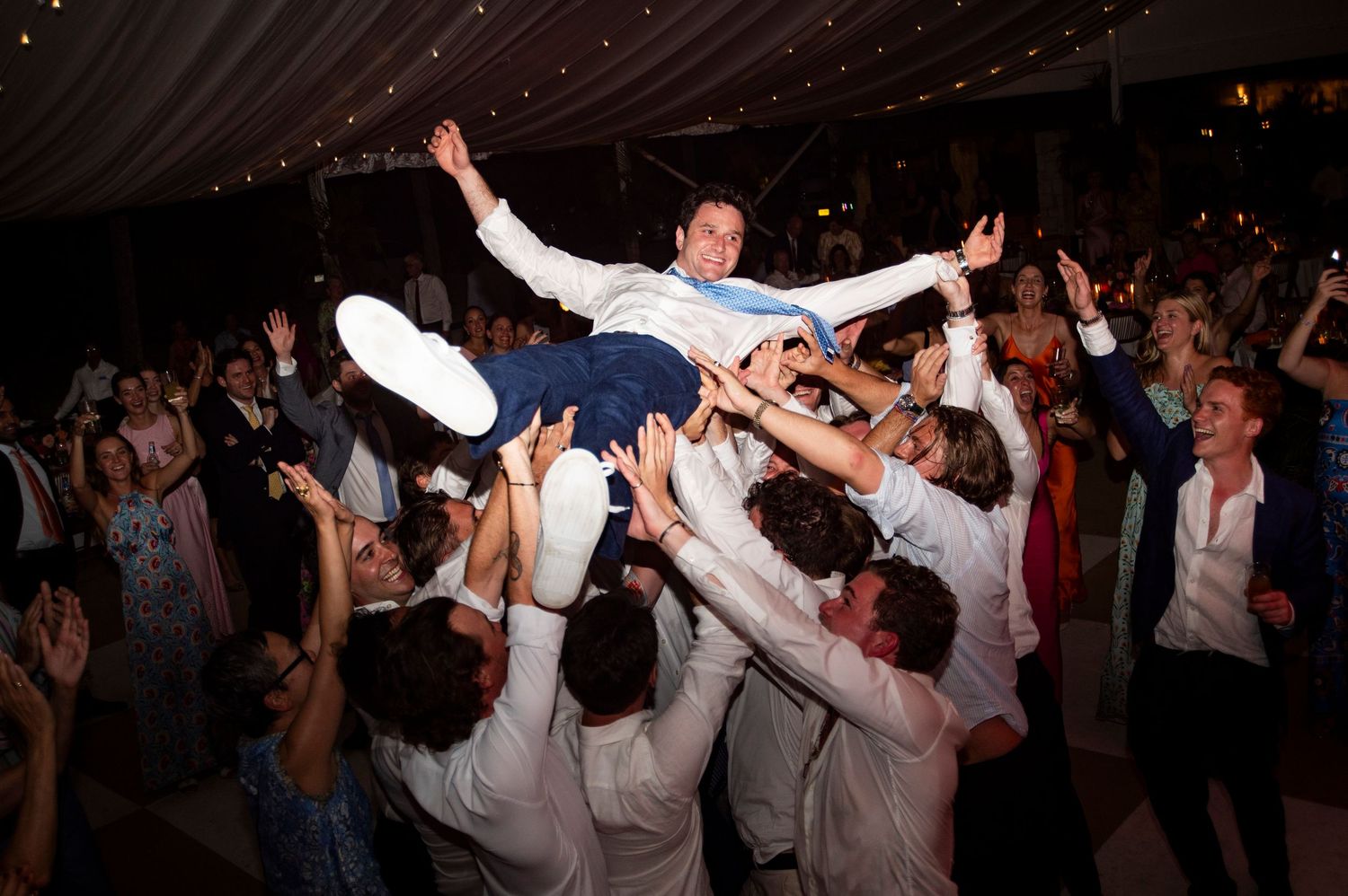Wedding reception dance party with guests celebrating under string lights.