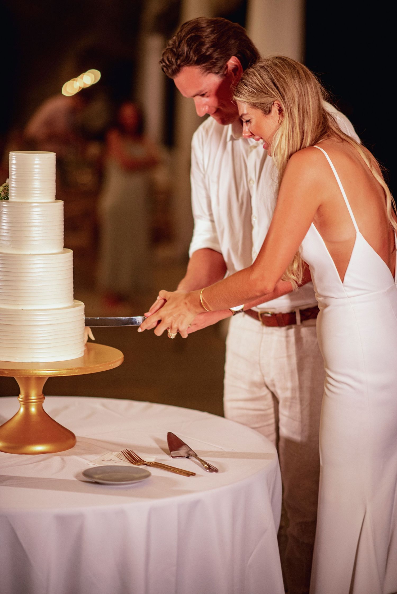 A couple in white attire cuts their elegant three-tiered wedding cake together at their reception.
