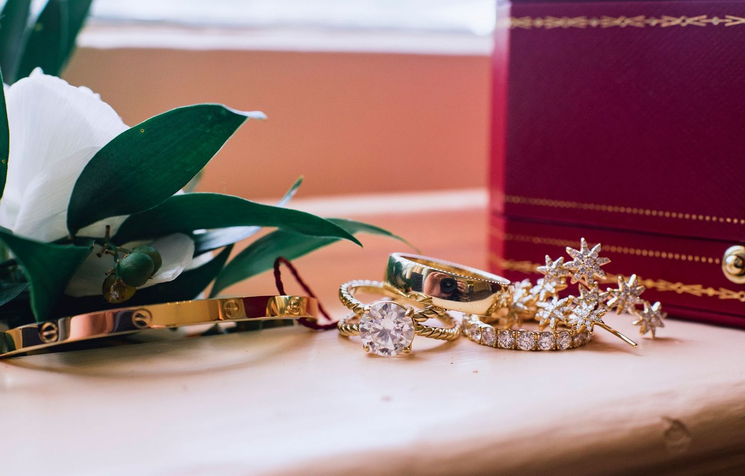 A delicate gold chain bracelet with small charms and green leaves arranged on a soft pink surface.