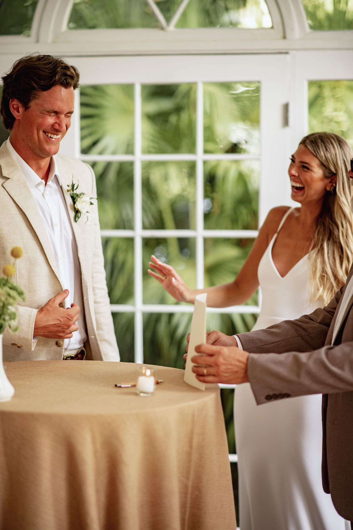 A joyful moment during a wedding reception with guests laughing together near a table with a candle.