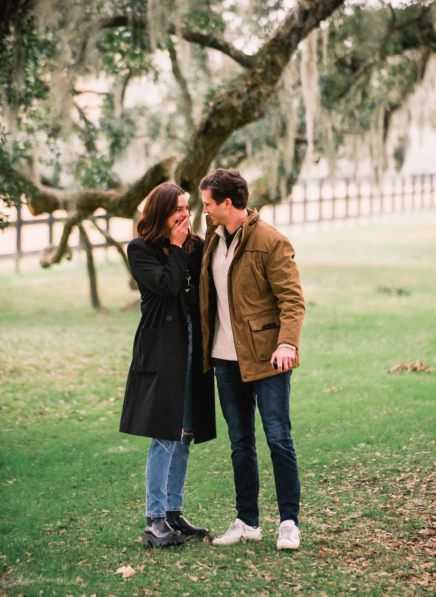 A couple shares tender moments while walking together on a grassy lawn with Spanish moss-draped trees in the background.