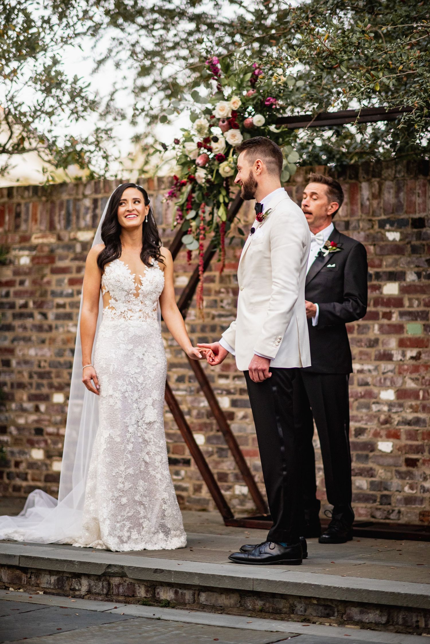 Newlyweds share a joyful moment together in front of a rustic brick wall during their outdoor wedding celebration.