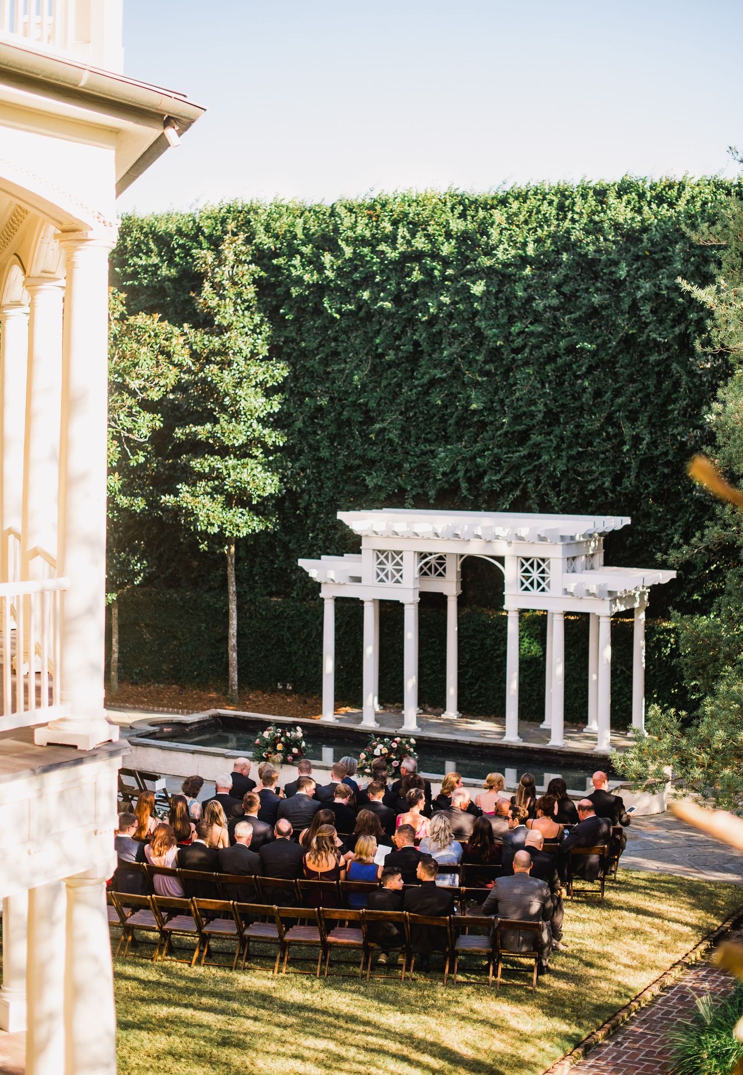Elegant white pergola and wooden chairs set up for an outdoor wedding ceremony in a lush garden setting.
