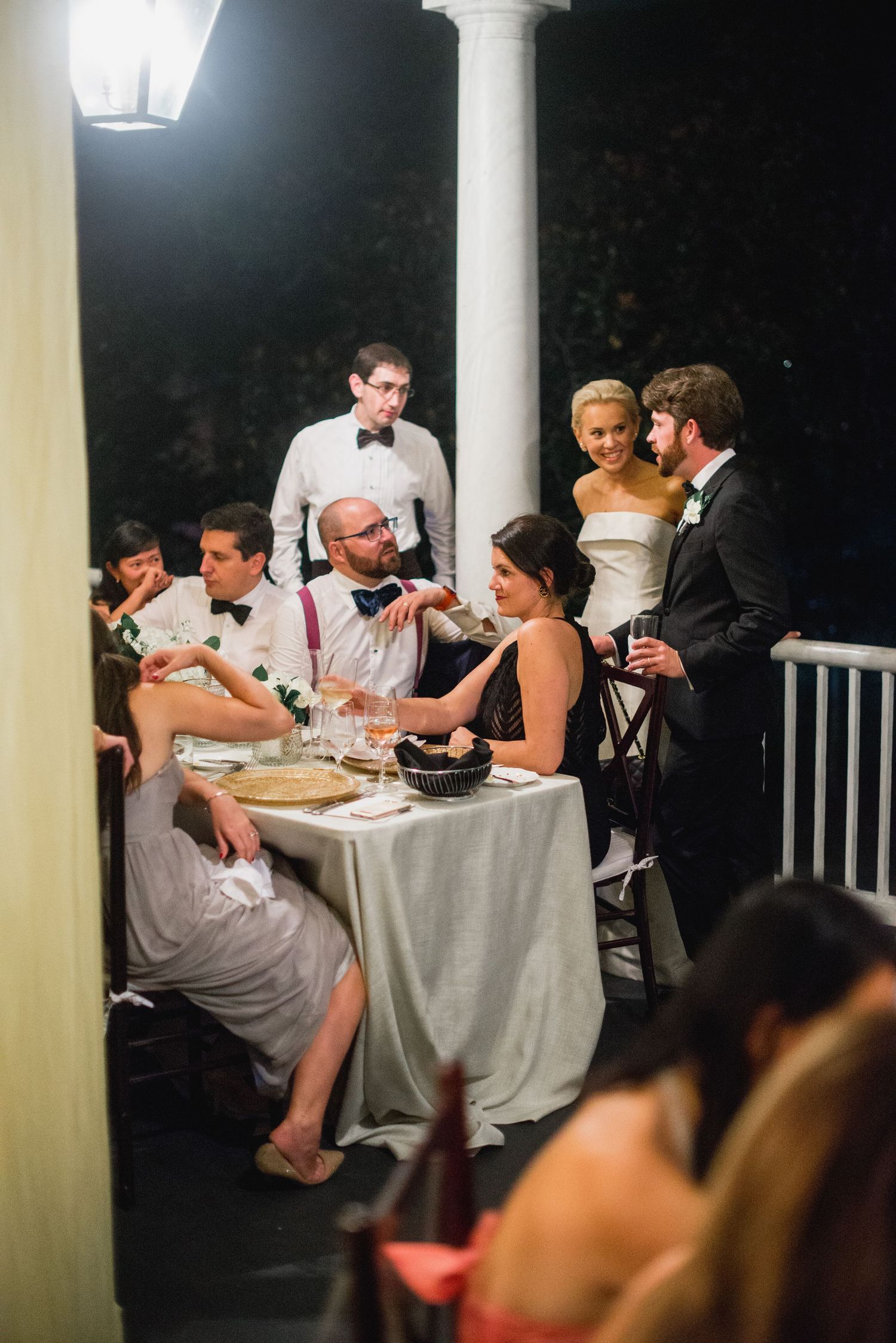 Wedding guests enjoy an intimate dinner reception on an elegant covered porch at night.