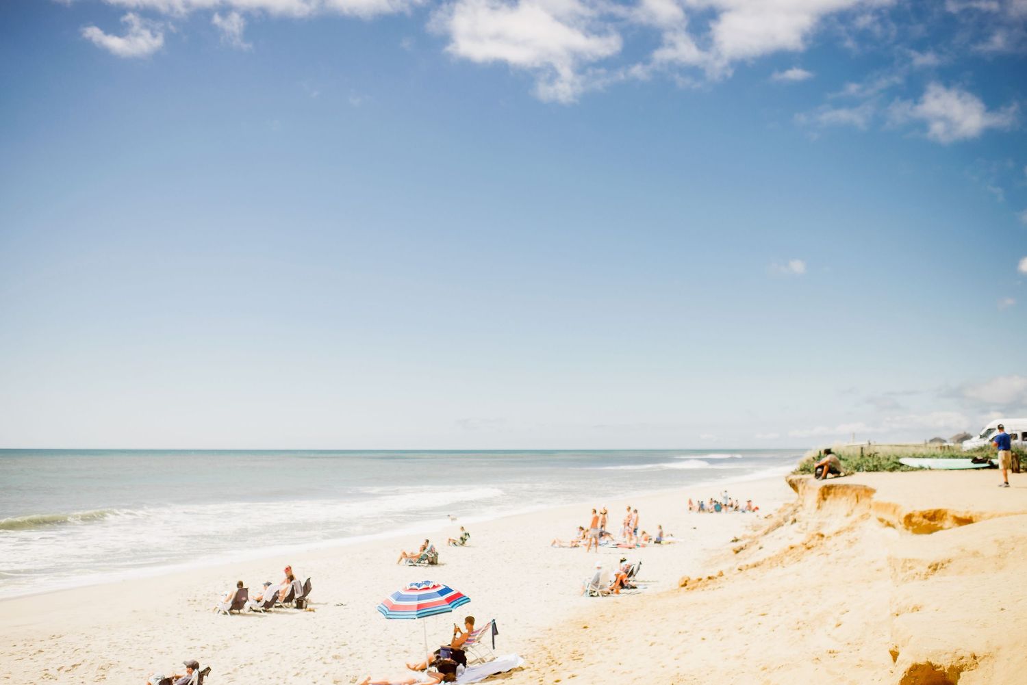 Summer beach scene in Nantucket with sandy shoreline, beach umbrellas, and gentle waves rolling in.