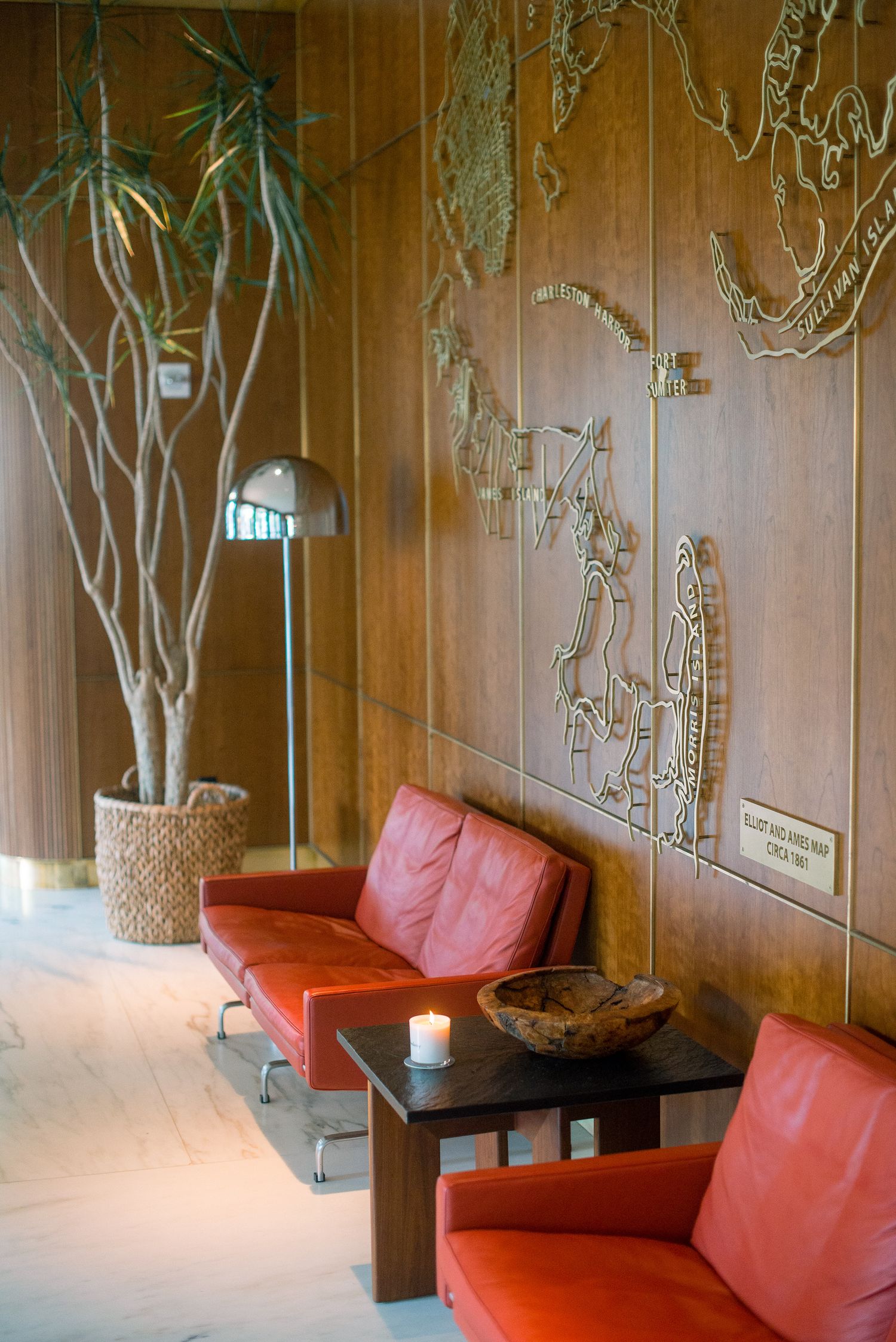 Modern lounge area with red couches and decorative wall art featuring tree designs against wooden paneling.