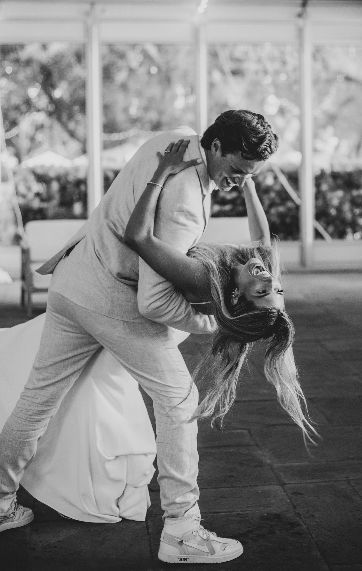 A couple in white outfits dances together in a romantic sequence of dips and spins on a dark floor.