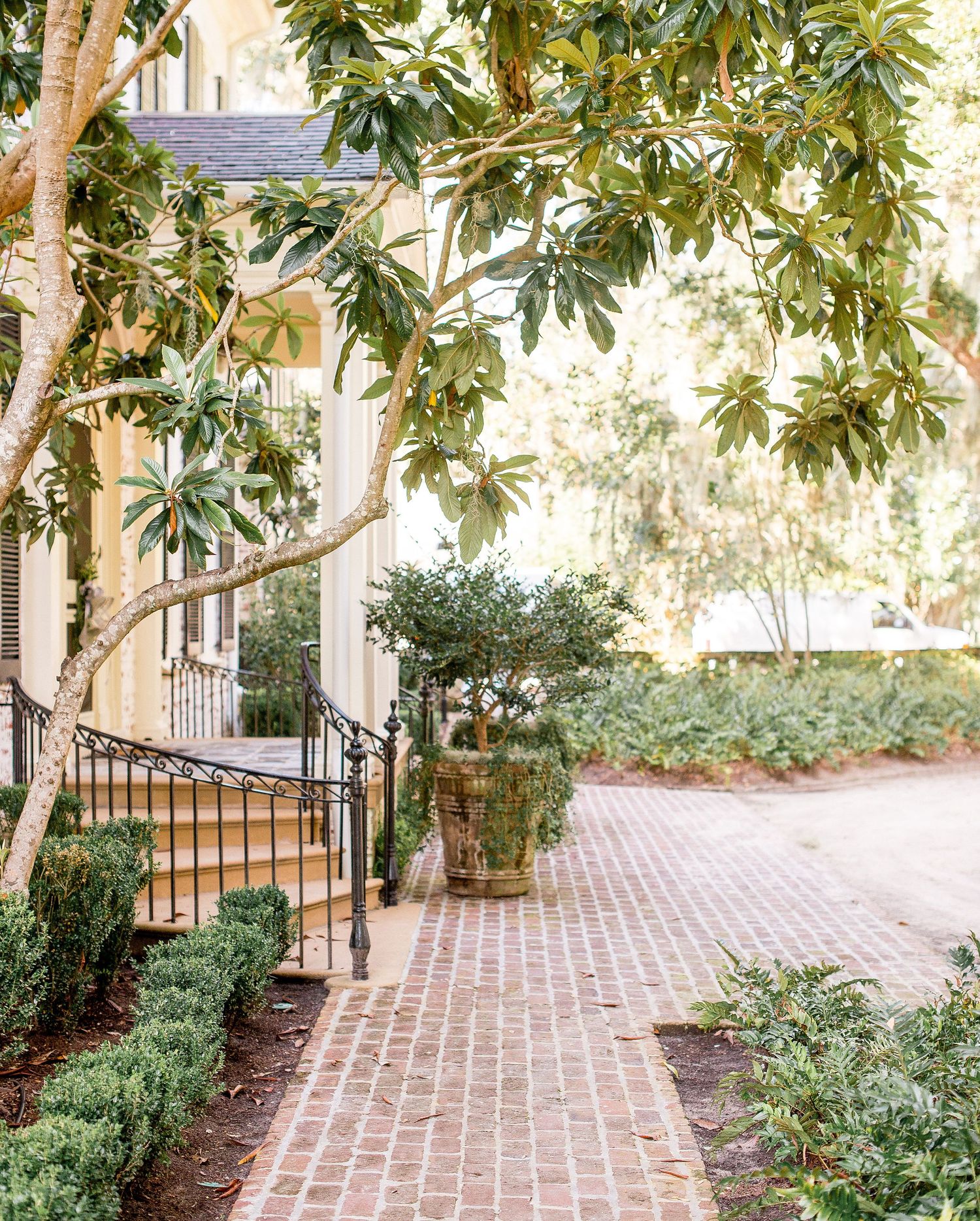 A curved brick pathway leads through a garden with magnolia trees and lush greenery creating a peaceful walkway.