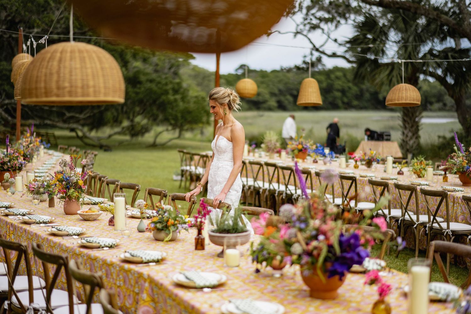 Elegant outdoor wedding reception table with woven pendant lights, rustic wooden chairs and colorful floral centerpieces.