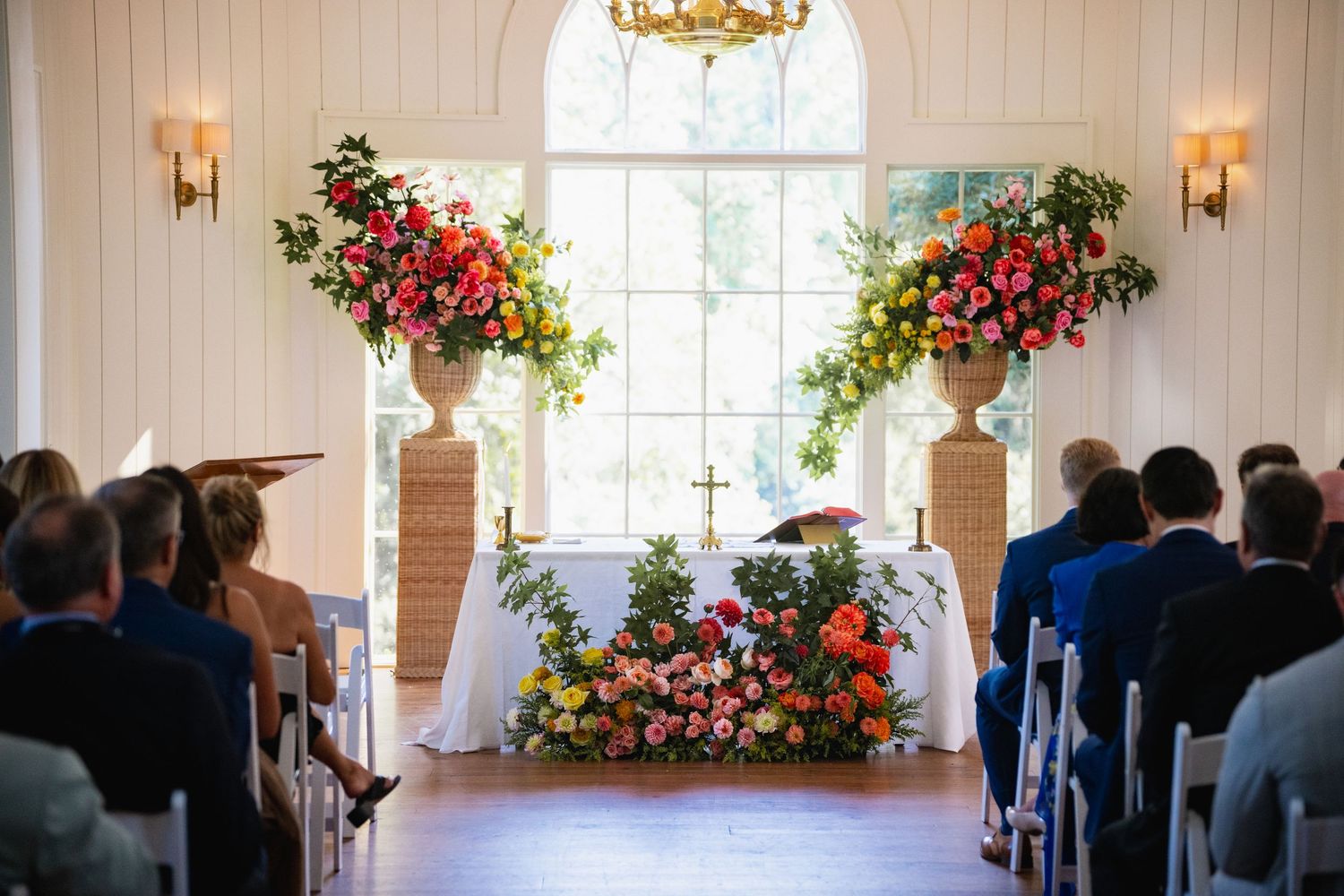 Beautiful wedding ceremony setup with pink and red floral arrangements decorating the altar in a bright chapel setting.