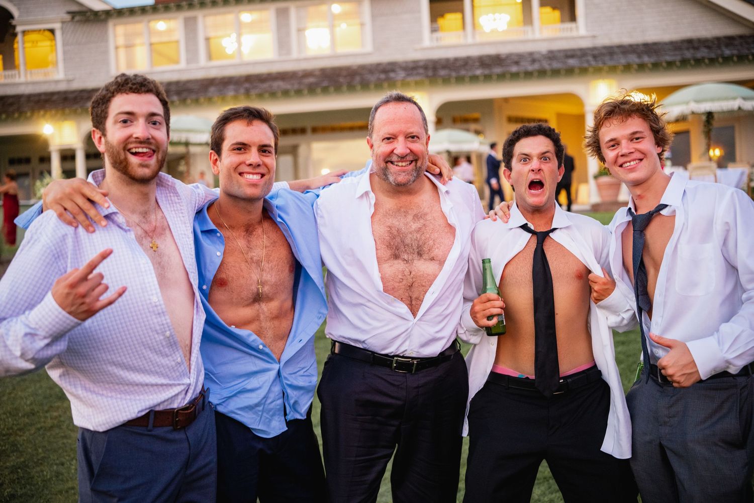 Group of wedding guests posing and celebrating outside venue at dusk.