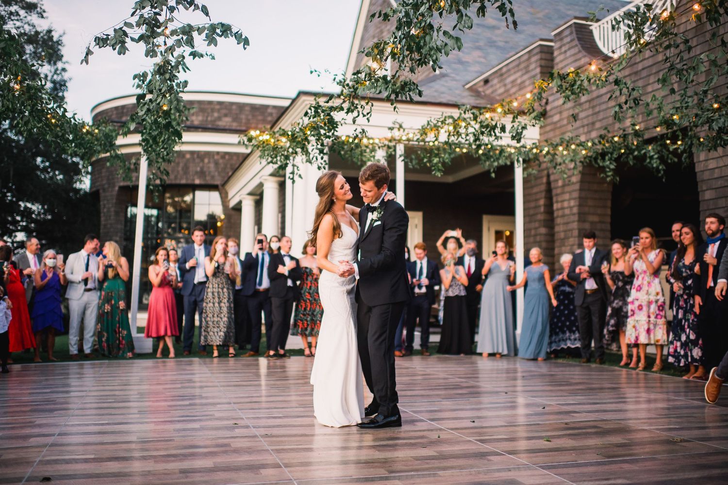 Guests dance and celebrate on a wooden dance floor during an elegant wedding reception at an indoor venue.