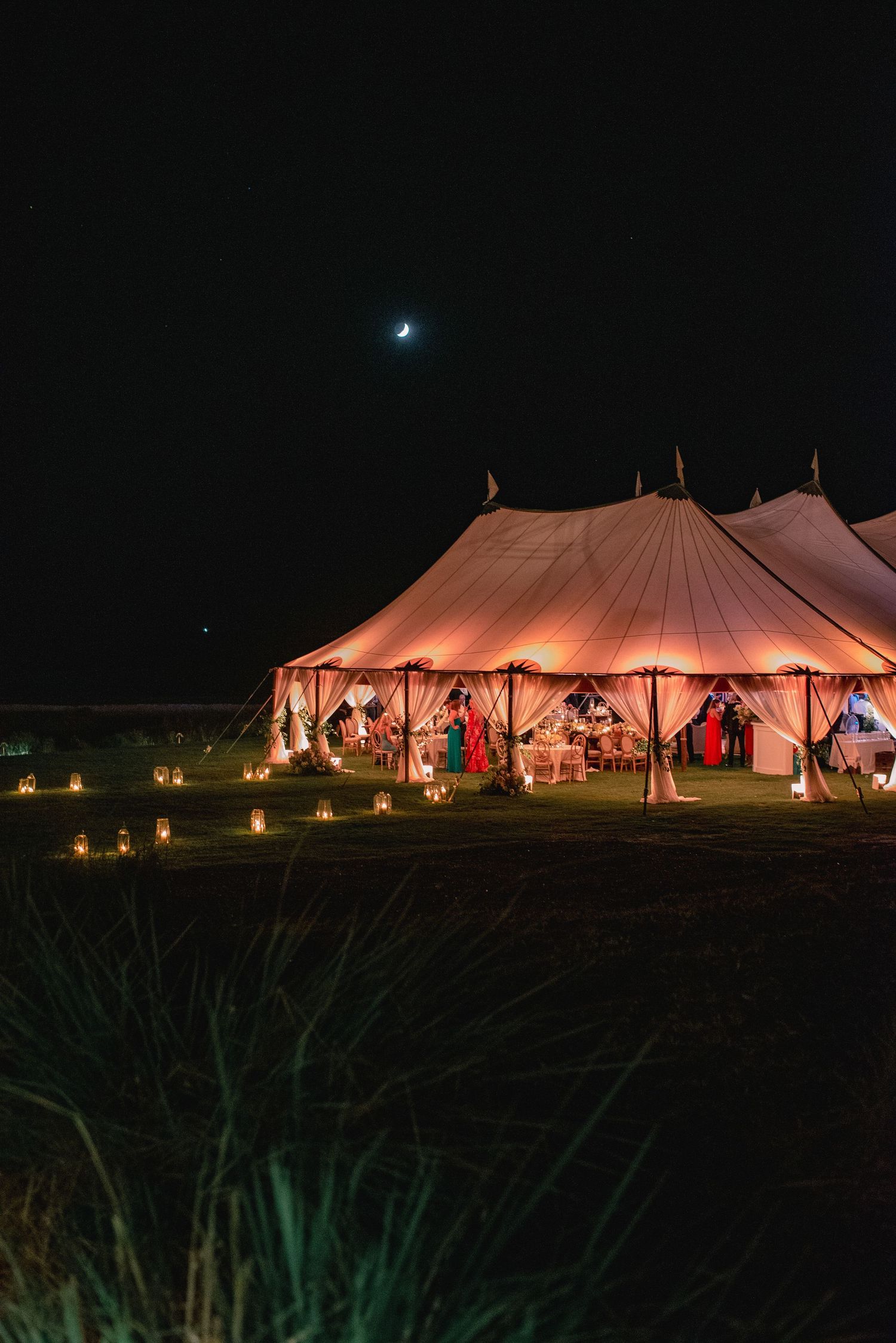 Illuminated white wedding tents glowing warmly at night with string lights creating a romantic outdoor reception atmosphere.