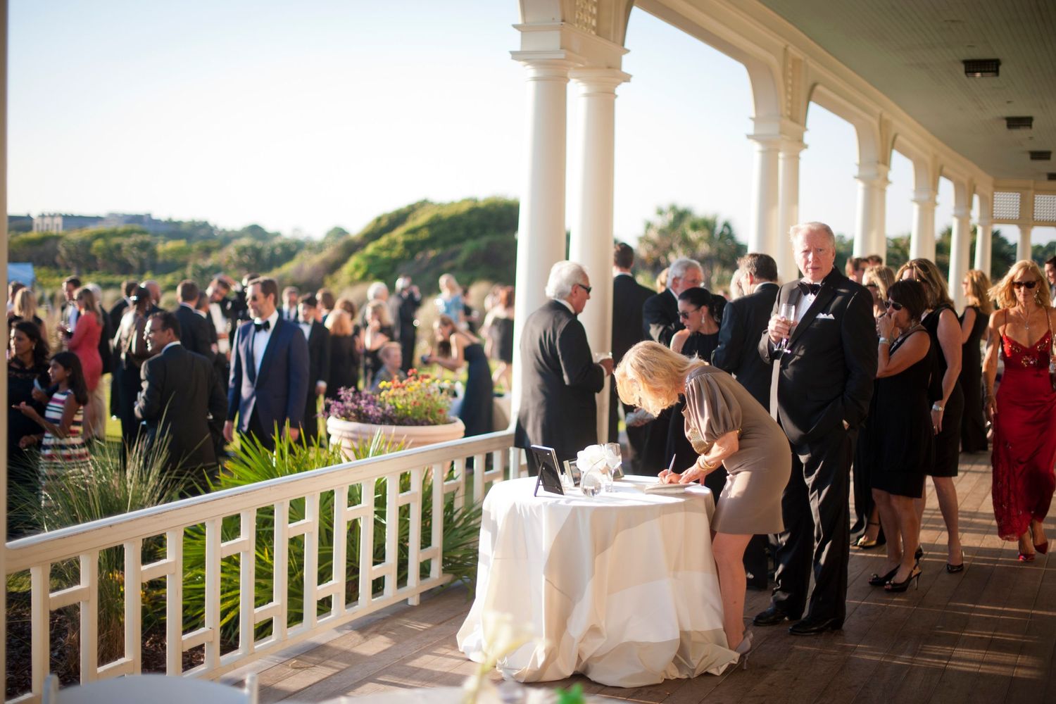 Wedding ceremony taking place on an elegant columned porch overlooking scenic grounds with guests gathered around.