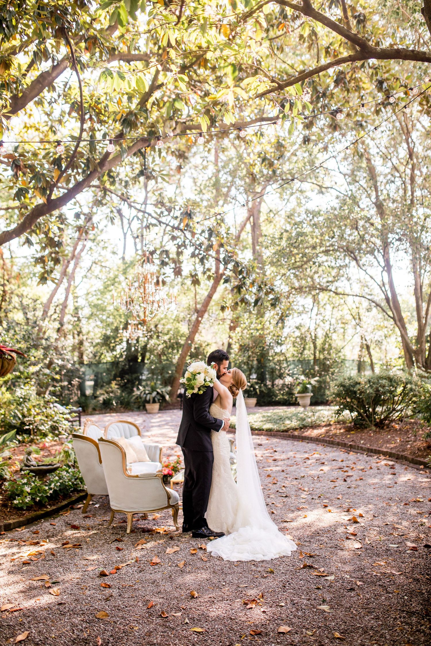 A romantic outdoor wedding scene with a vintage white sofa under autumn trees in a wooded garden setting.