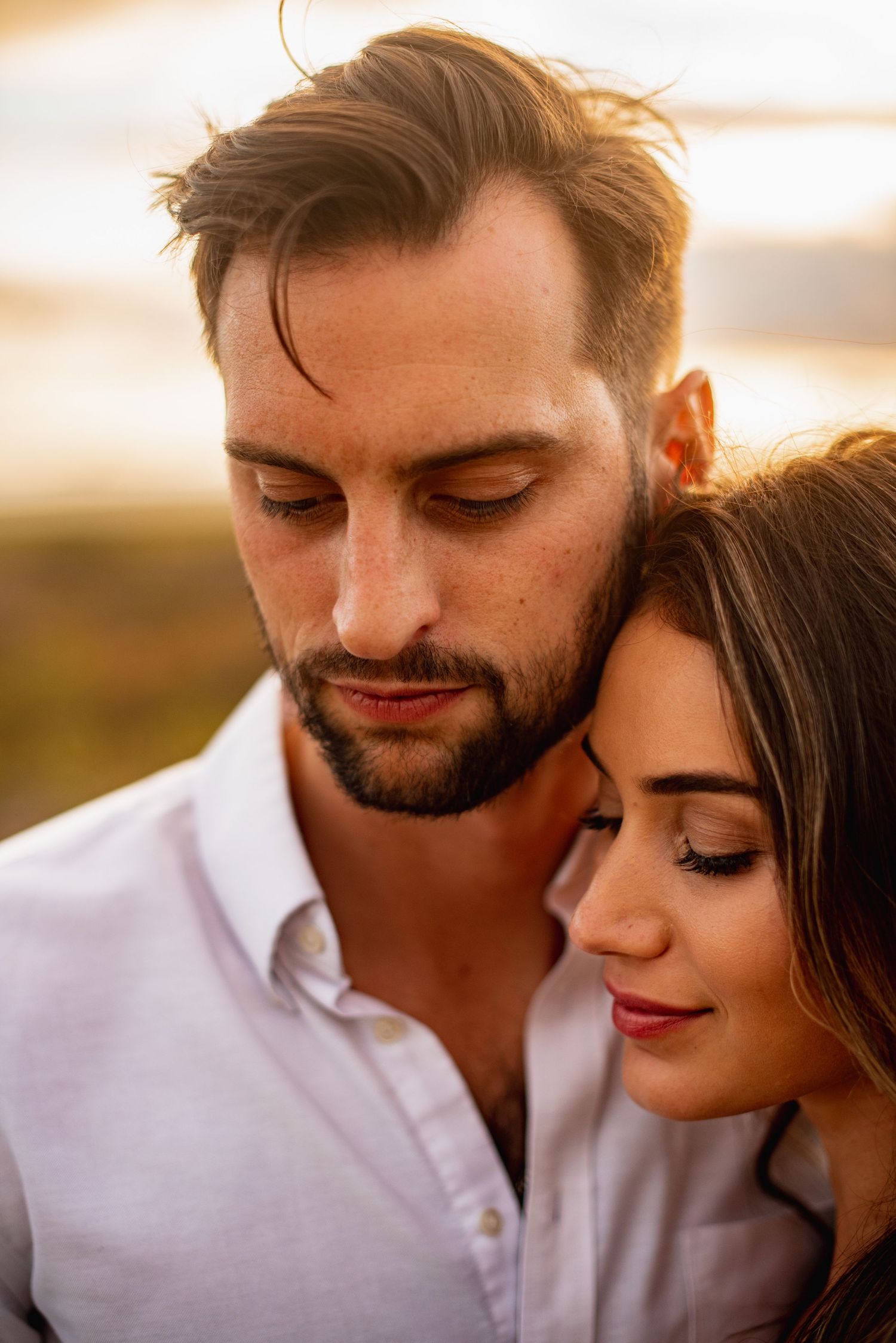 A romantic couple shares an intimate moment together at sunset, with soft golden light illuminating their faces.