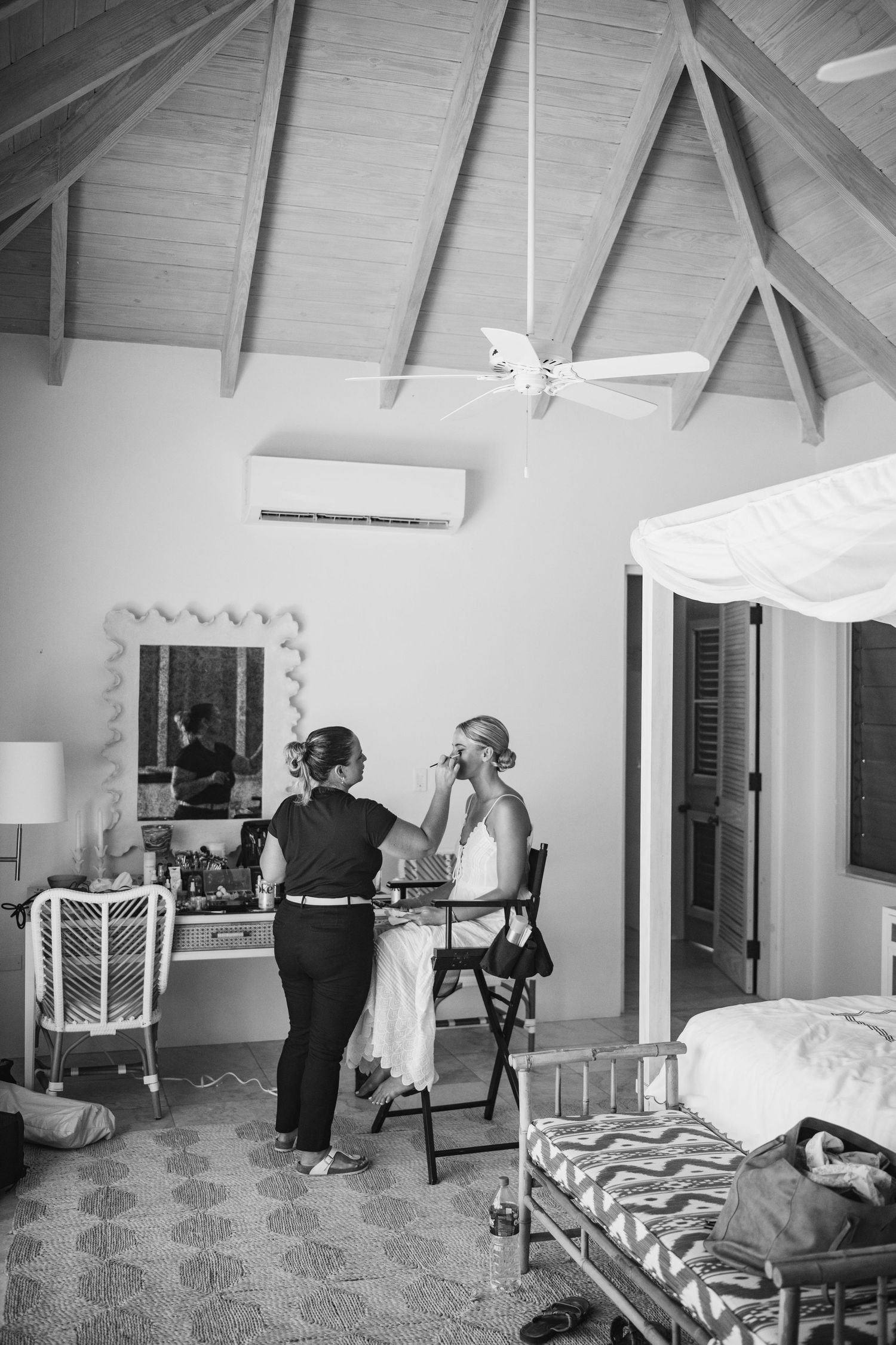 Black and white photo showing a preparation scene in a room with vaulted ceilings and a ceiling fan.