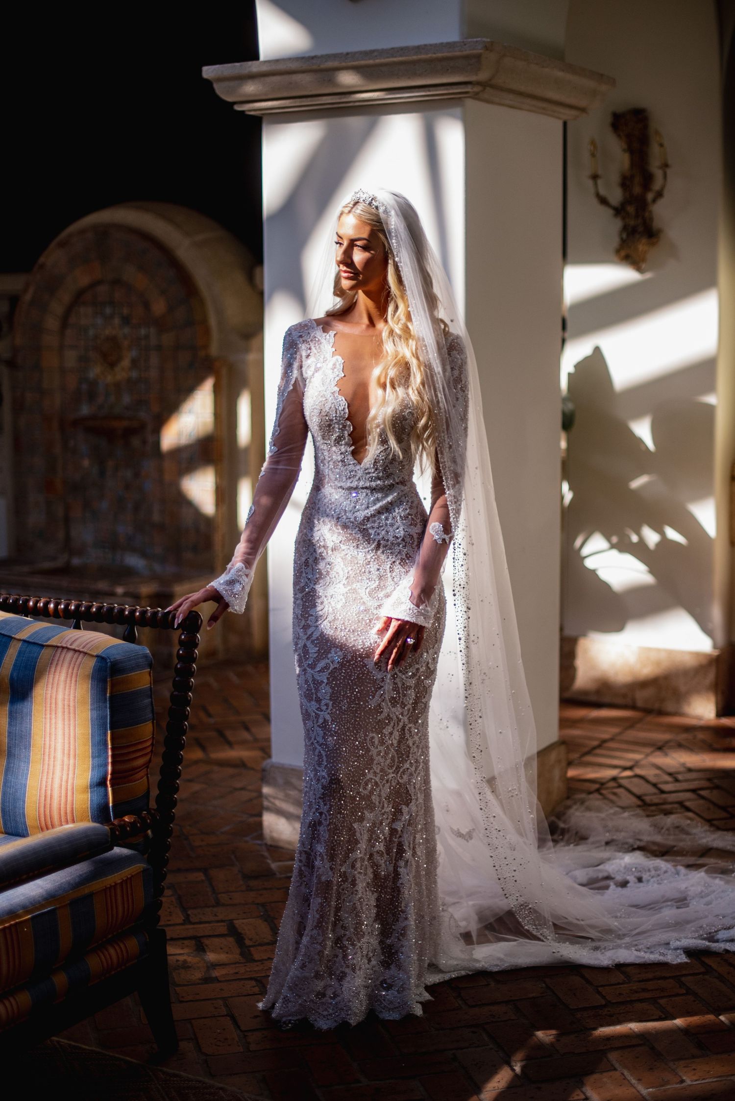 A bride in a sparkling sequined wedding gown stands in dramatic window light creating ethereal bridal portraits.