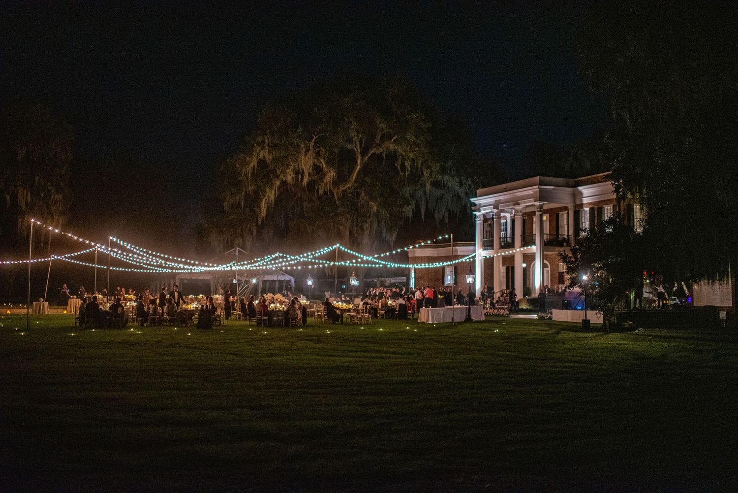 String lights illuminate a dark outdoor venue with buildings and trees silhouetted against the night sky.