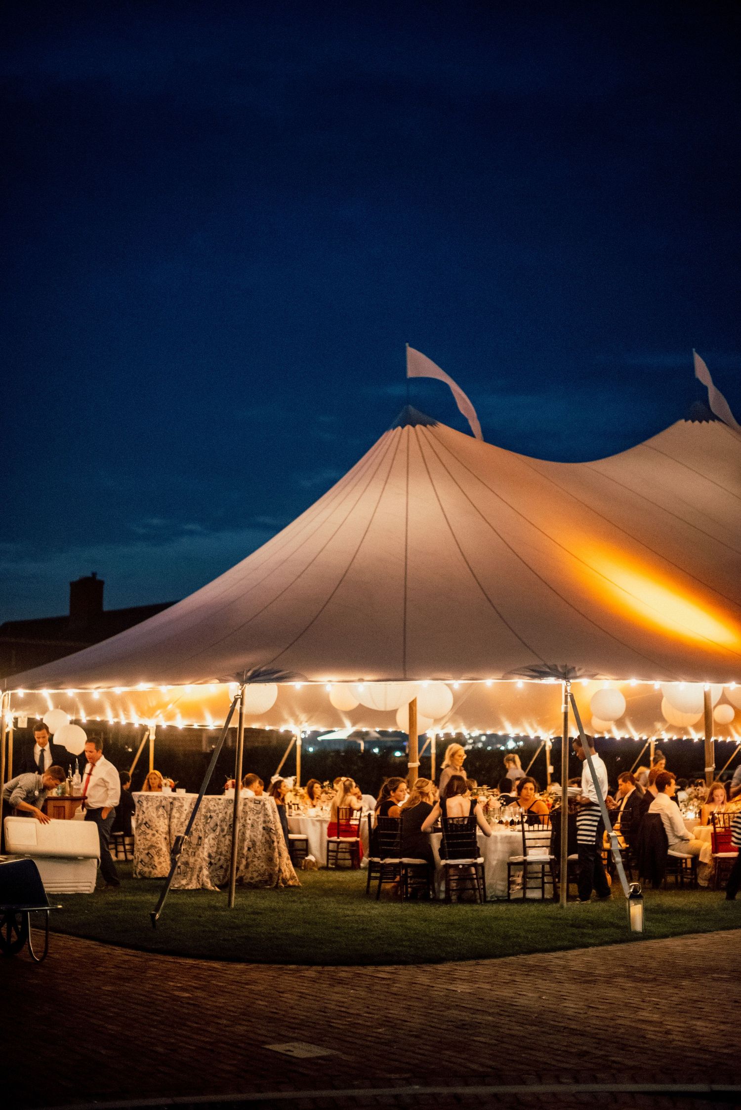Large white wedding tent illuminated at night with warm lighting and guests inside.