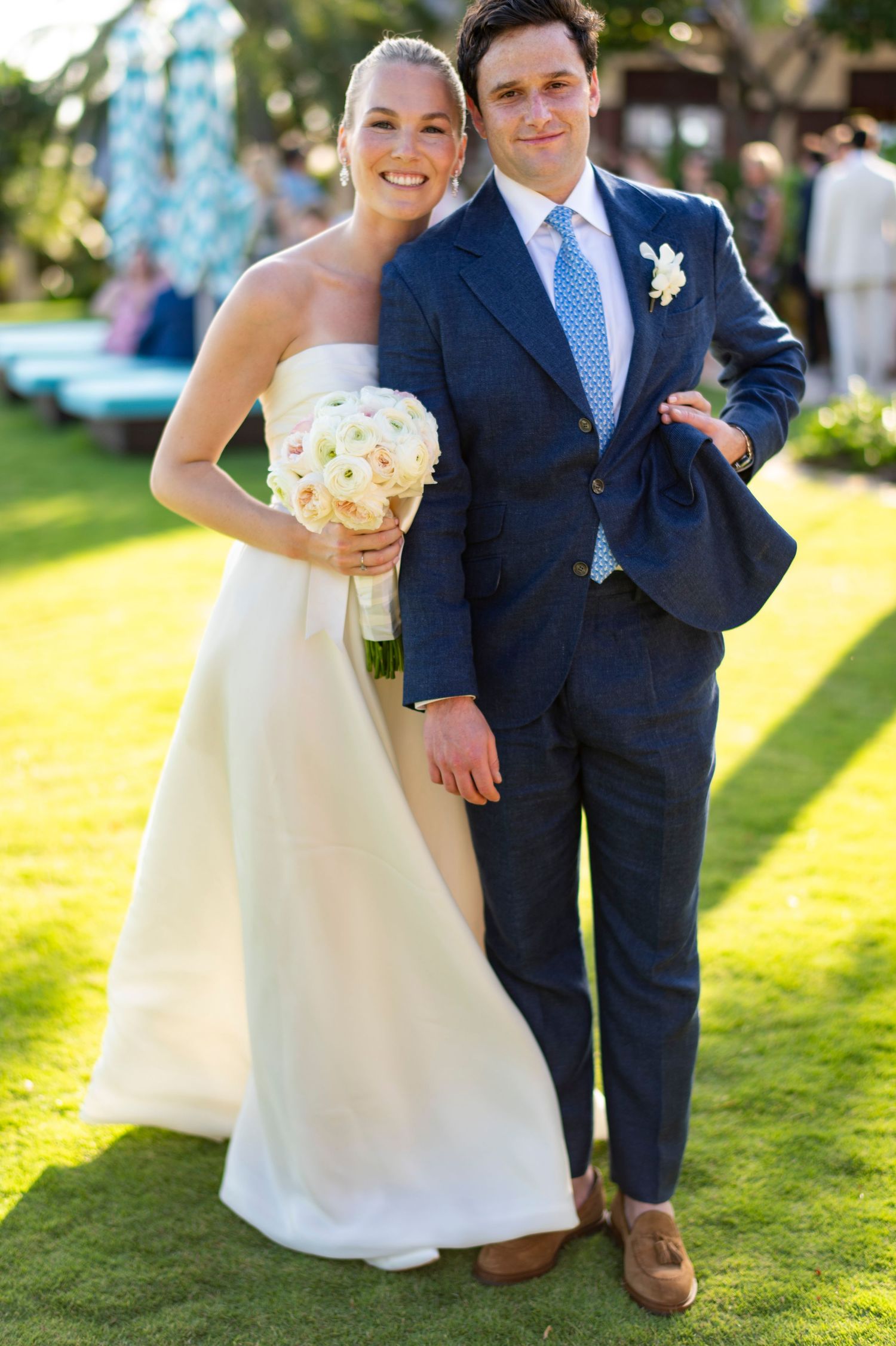Wedding couple poses on sunny lawn with elegant attire and natural backdrop.