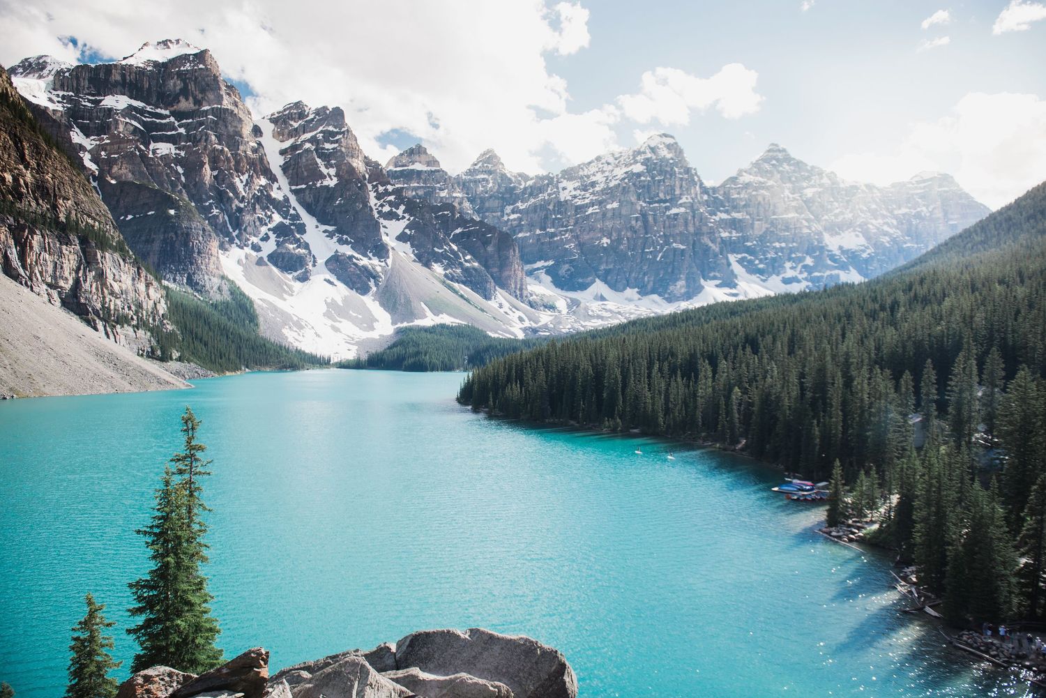 Panoramic vista of a turquoise alpine lake surrounded by snow-capped mountain peaks.